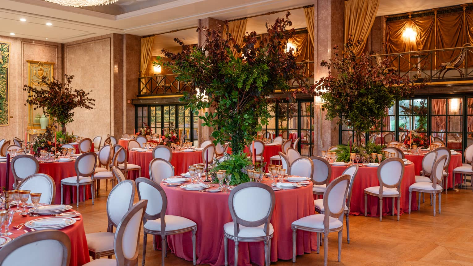Elegant ballroom set for a formal event, with table rounds featuring coral-coloured tablecloths and tall floral centrepieces
