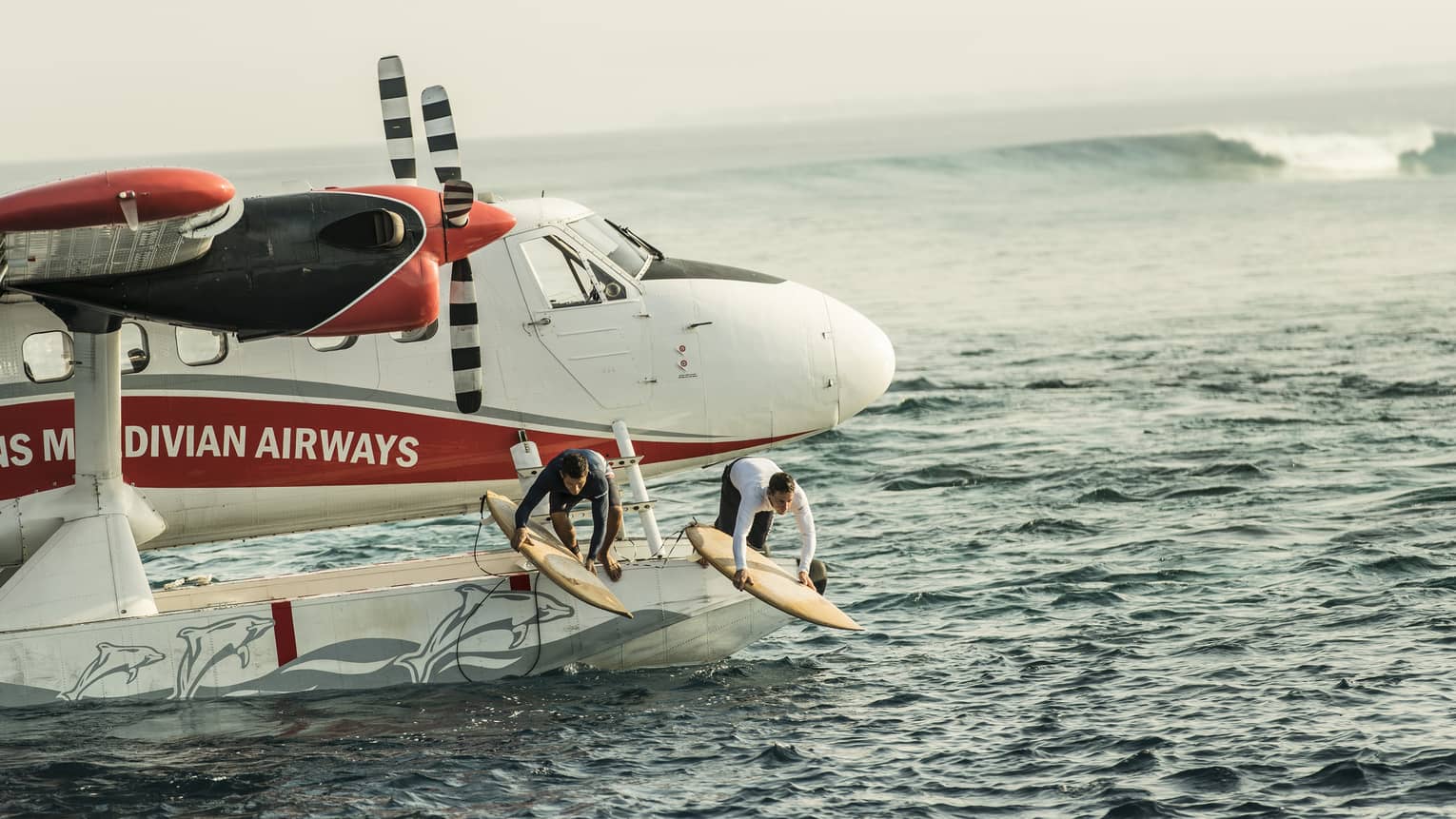 Two people with surfboards jump from float plane onto waves