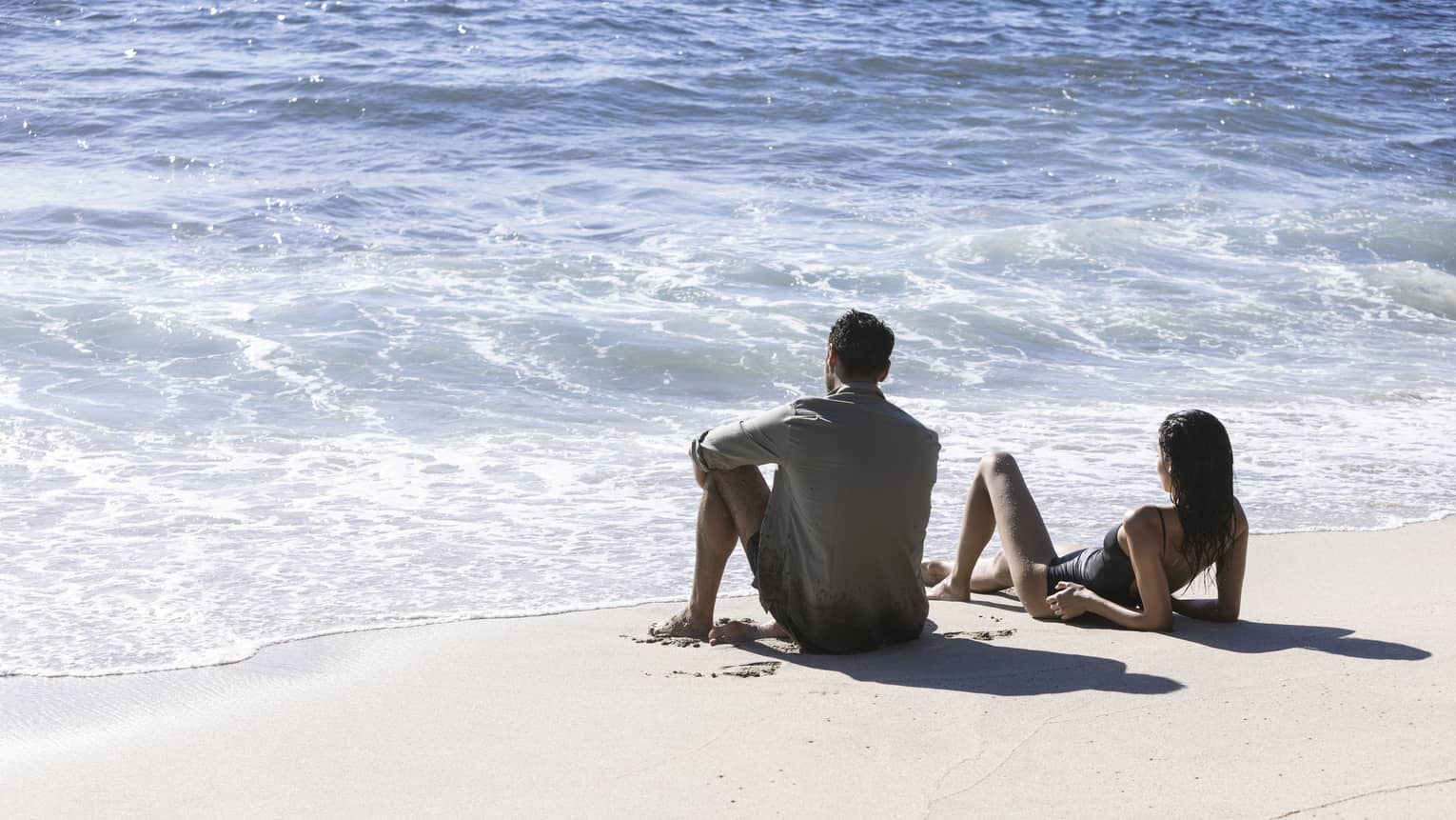 A couple lounges oceanside on a beach