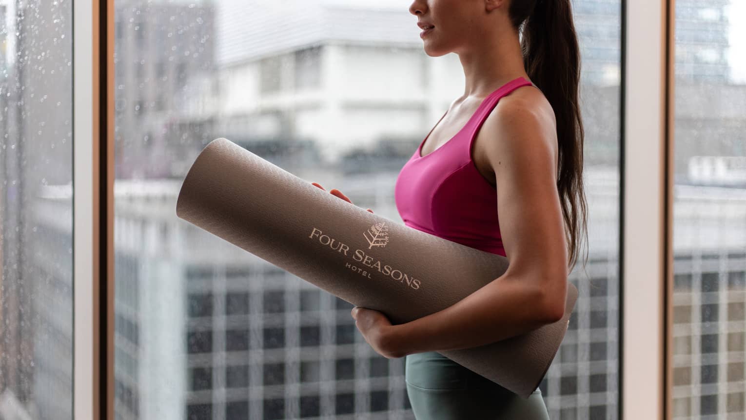 Woman in workout gear holds rolled yoga mat with Four Seasons logo