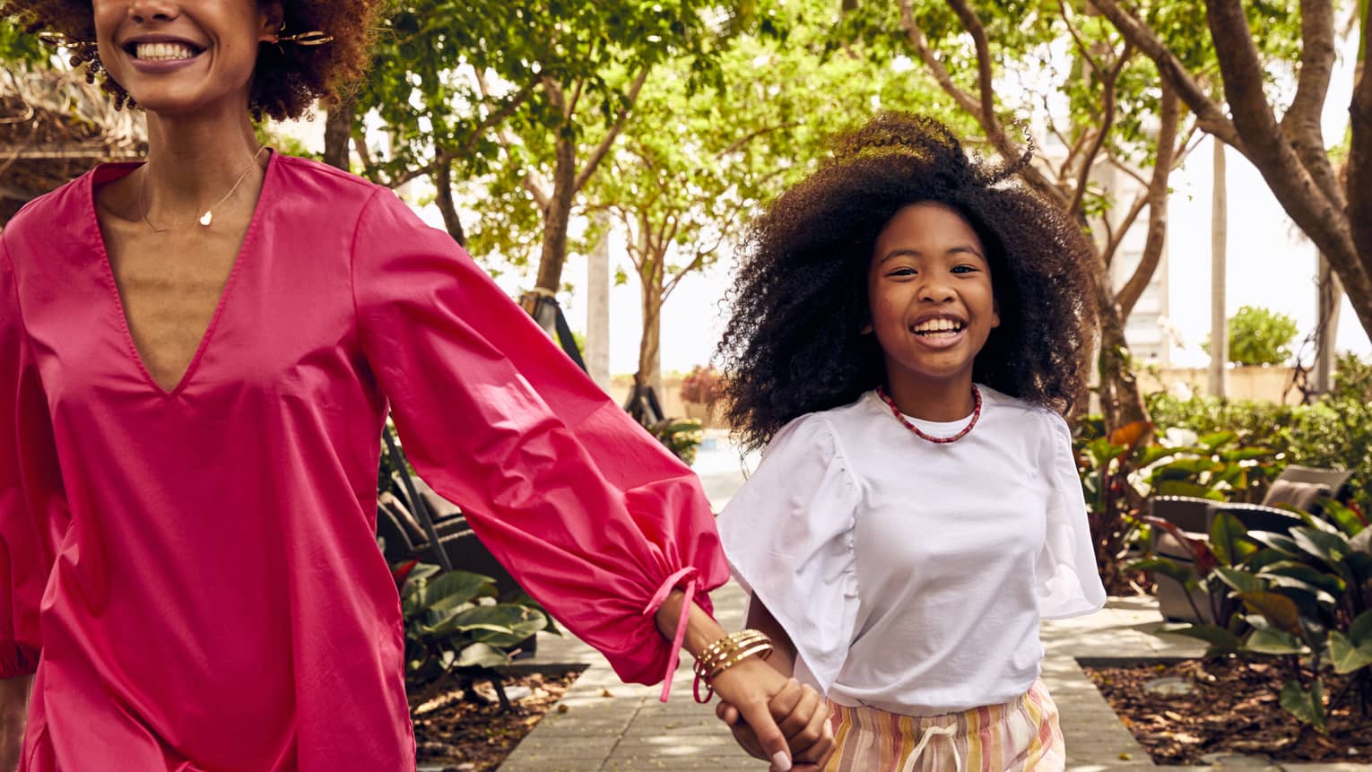 Woman and young girl walk hand in hand on sidewalk