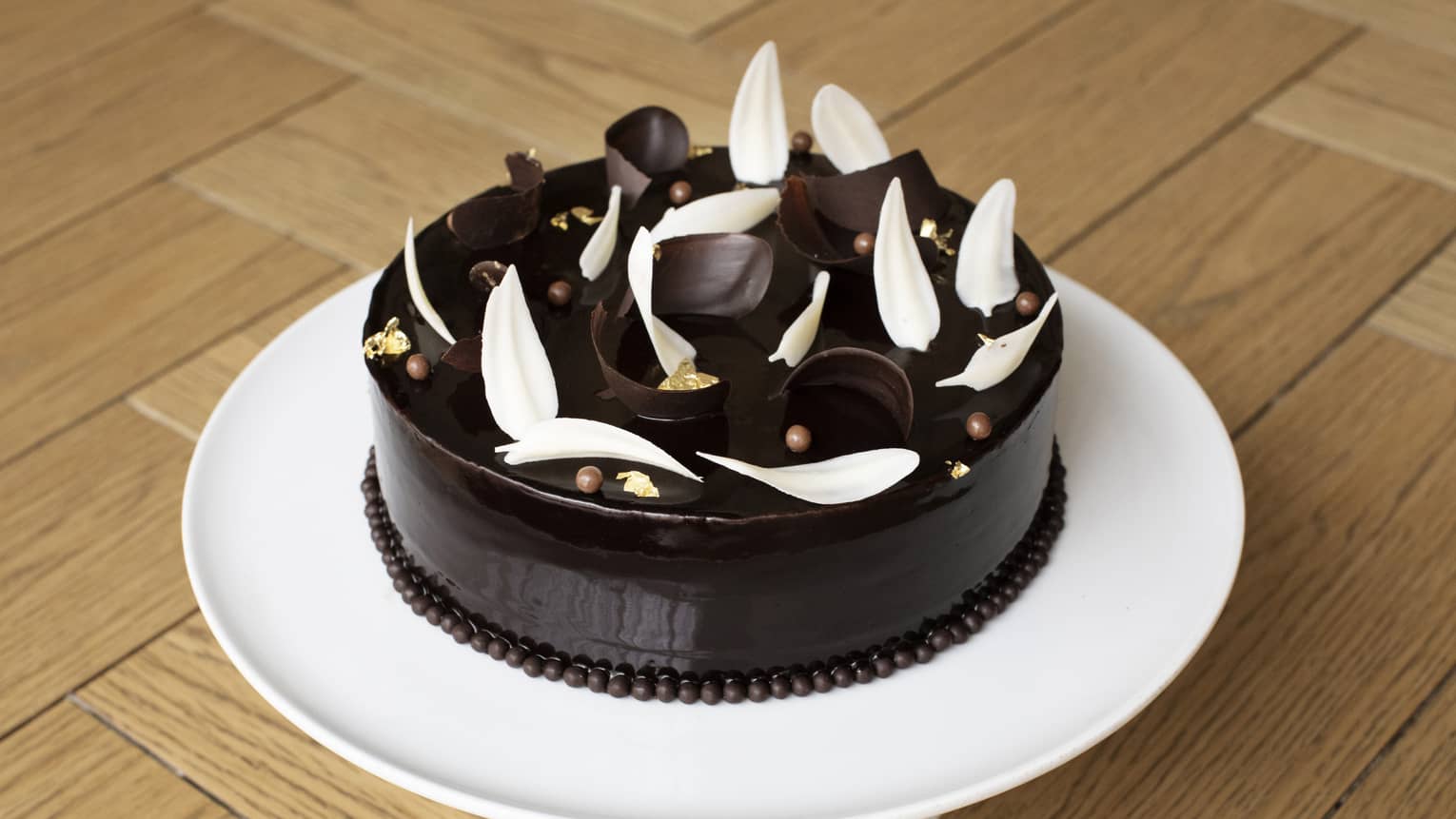 Chocolate cake with slices of chocolate on top on a white platter.