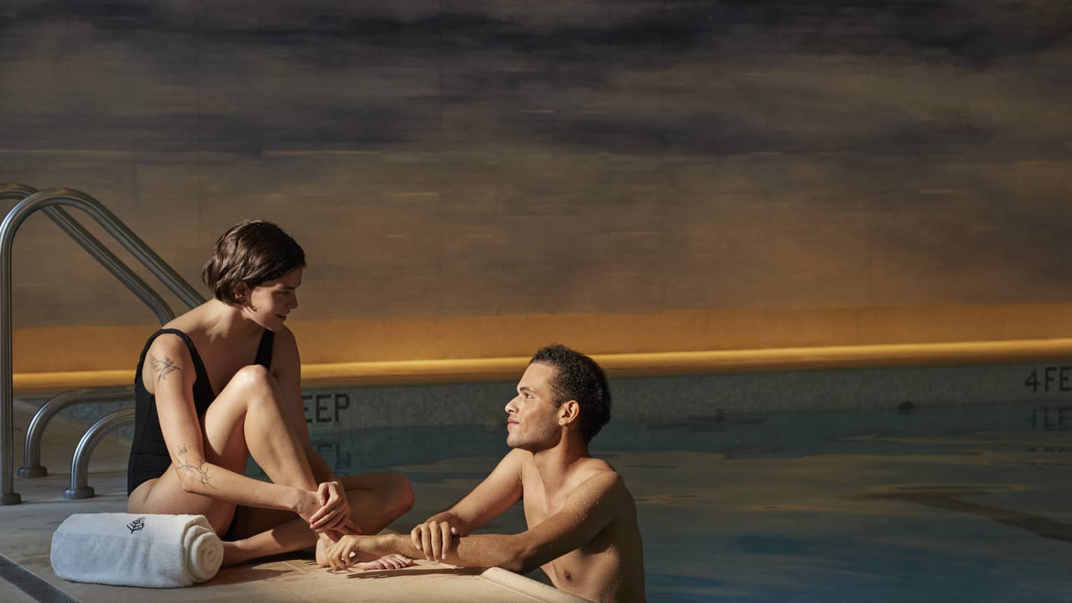 Person sitting poolside with a towel talking to another person leaning on the edge of the pool at Four Seasons luxury hotel