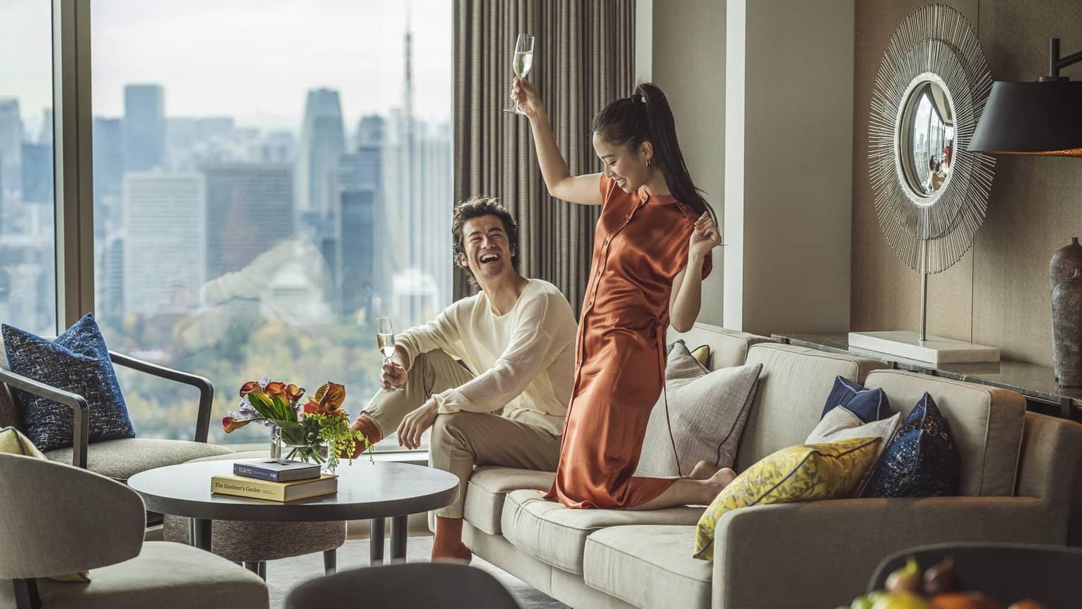 Laughing couples relaxes with glasses of champagne in living area with city views