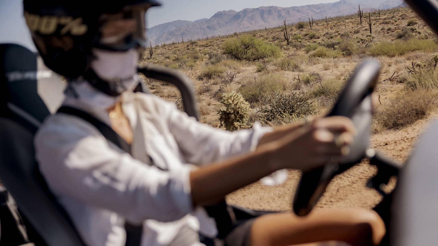 Person wearing a helmet and driving a car with no doors with mountains in the background.