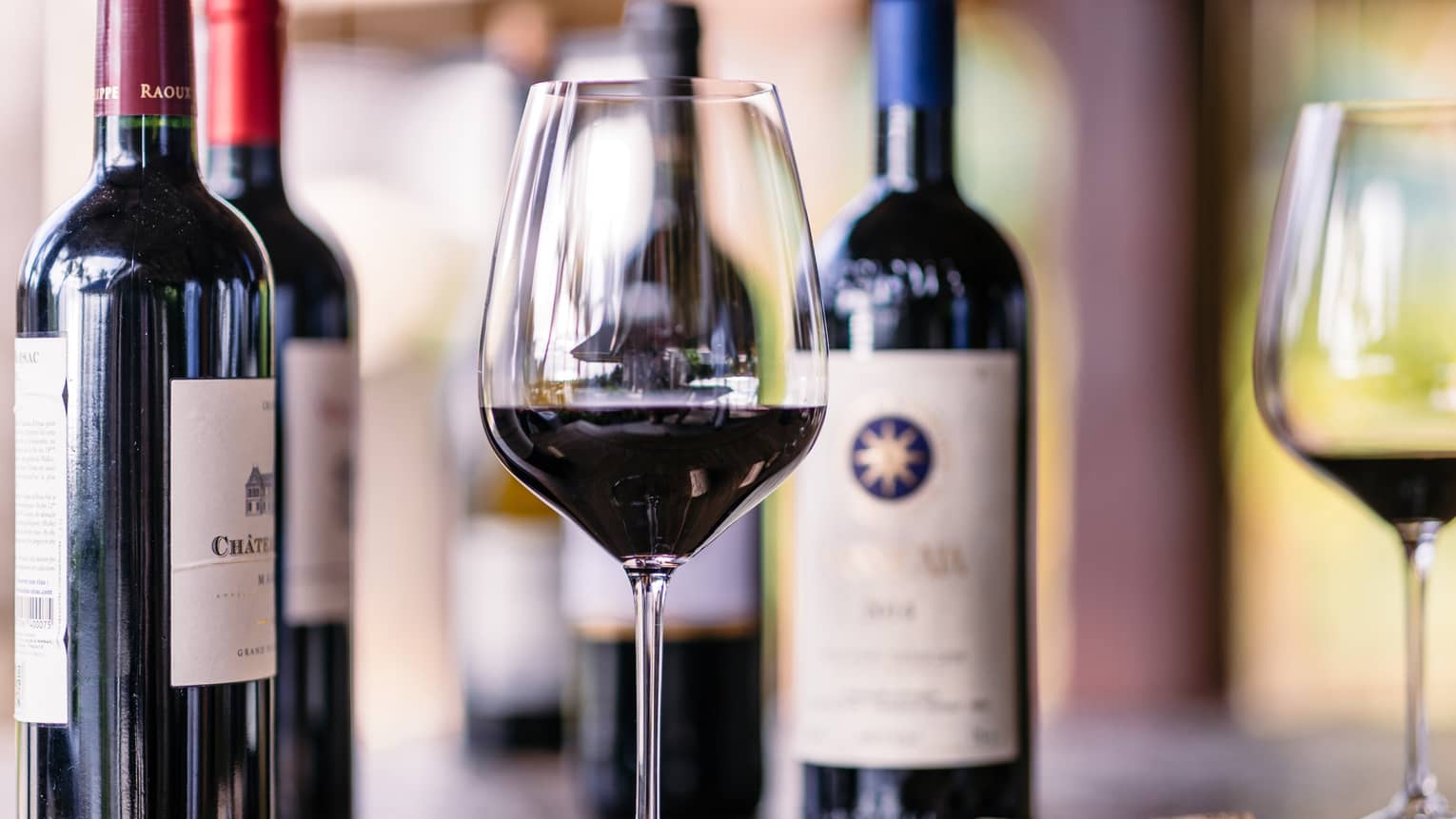 Closeup of glass of red wine, bottles beside it