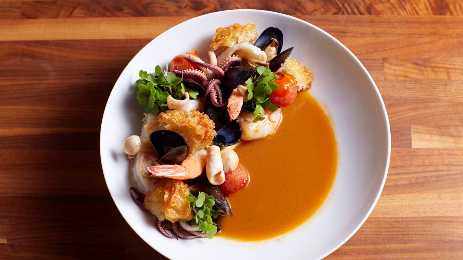 Aerial view of white dish with mixed seafood prawns, mussels, clams, scallops and calamari in red broth