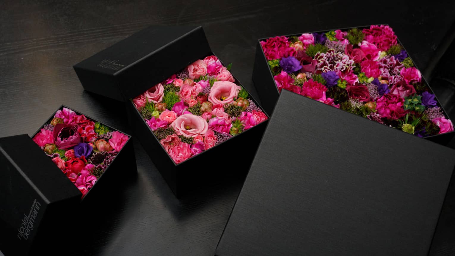 Three arrangements of brightly coloured flowers in sleek black boxes