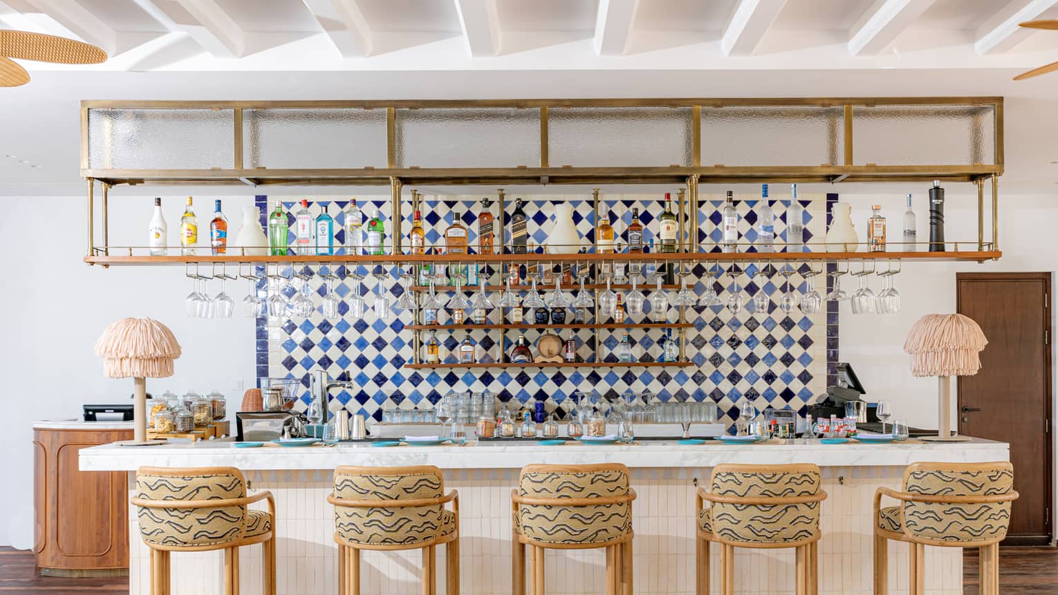 Restaurant bar lined with five bar stools underneath open shelving lined with liquor bottles