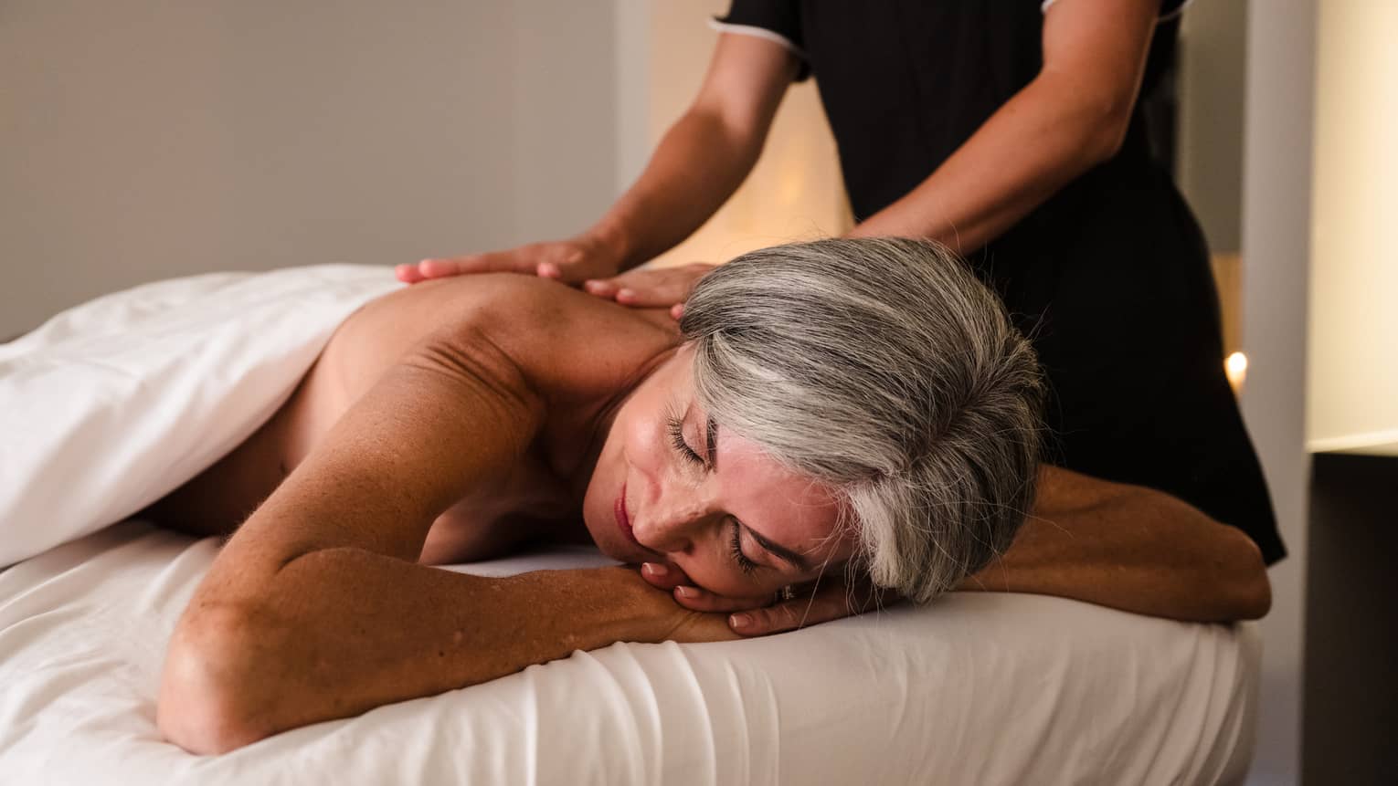 Person lies face down on massage table as therapist in black uniform performs massage