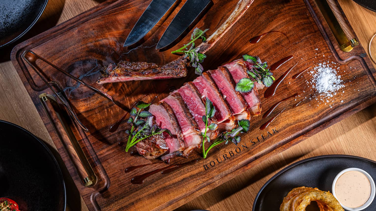 A cutting board with meat cut into slices and plates of side dishes.