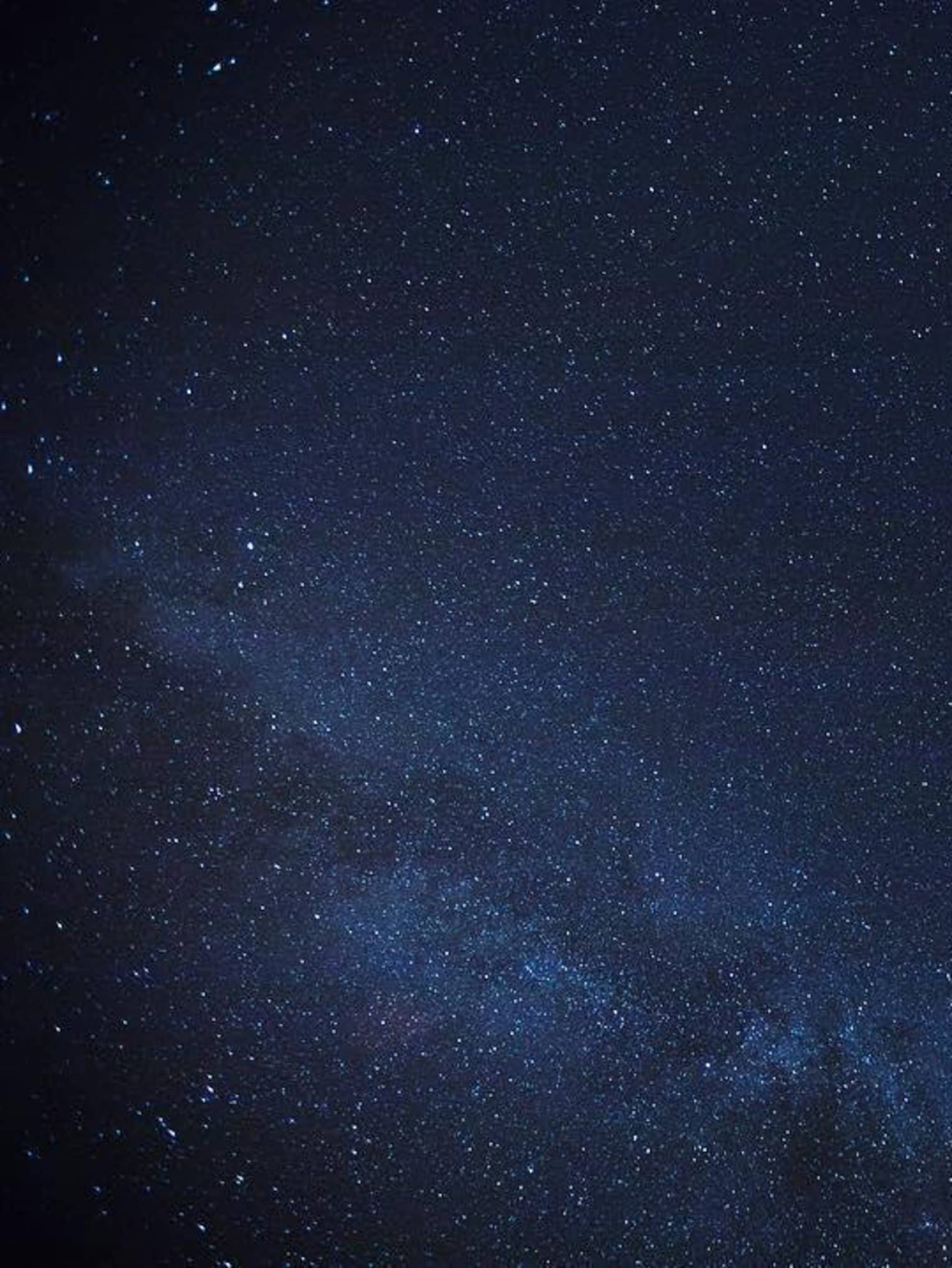 Thousands of stars dusting across a clear night sky; a cluster of stars form the Milky Way, just barely visible in the sky.
