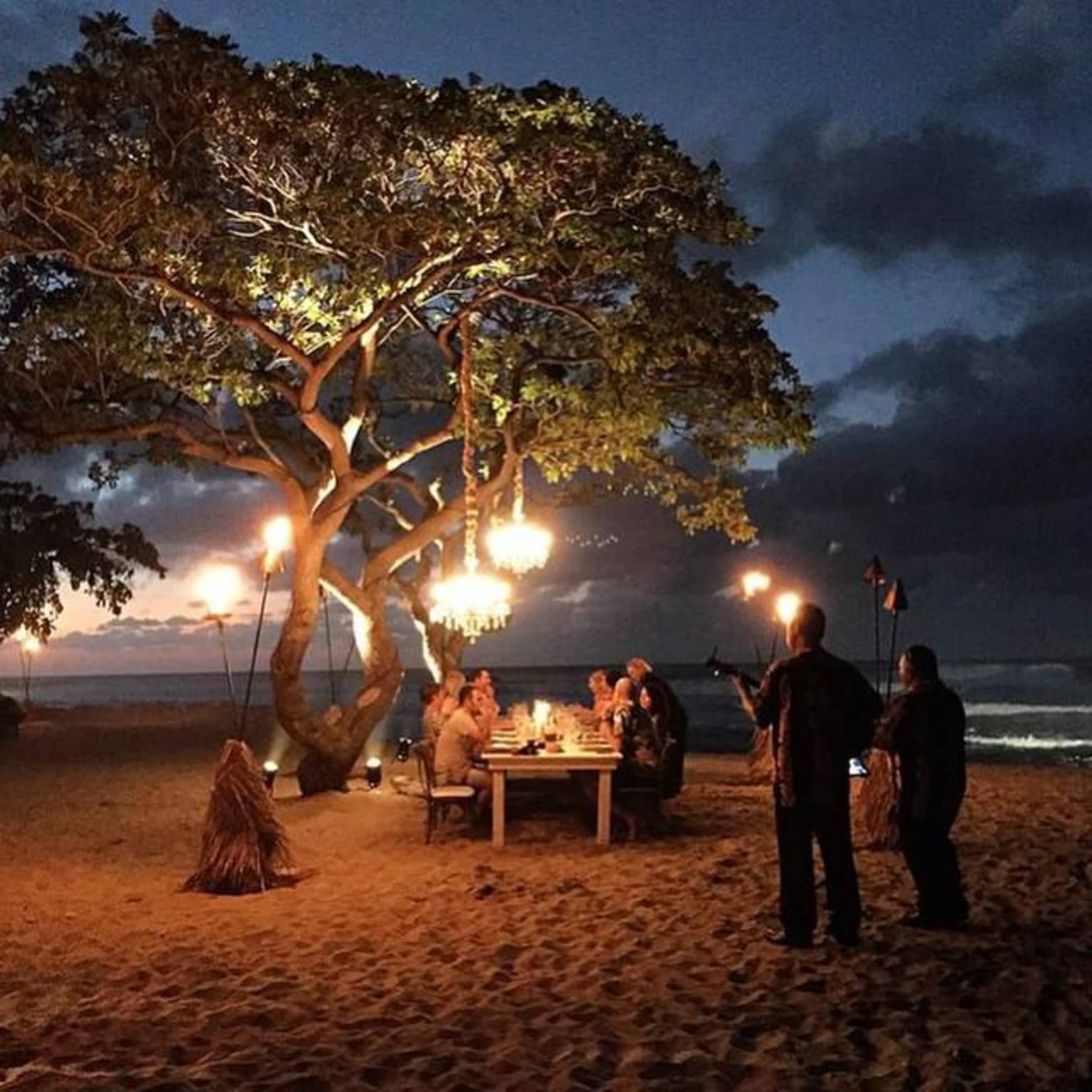 Musicians play for a table of guests enjoying dinner on the beach at sundown.