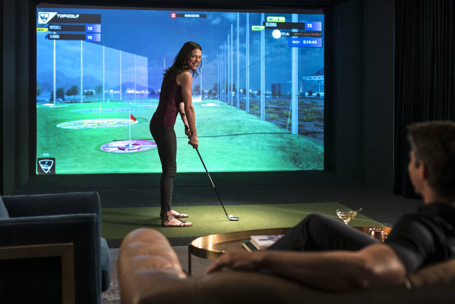 A woman prepares to swing a golf club in front of a virtual golf simulator screen
