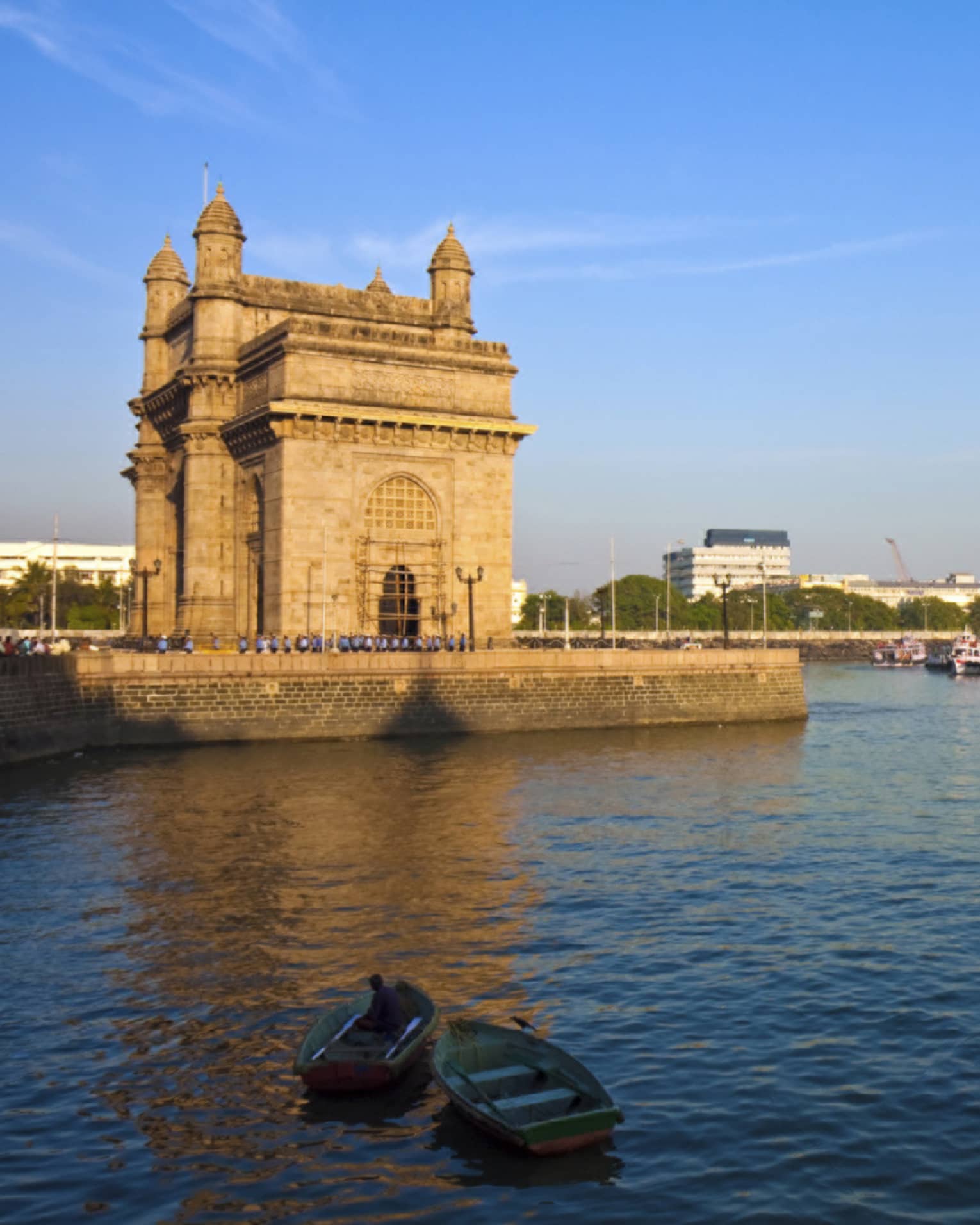 Harbourside view of an imposing towered stone structure, scattered rowboats in the foreground, larger moored ships beyond.