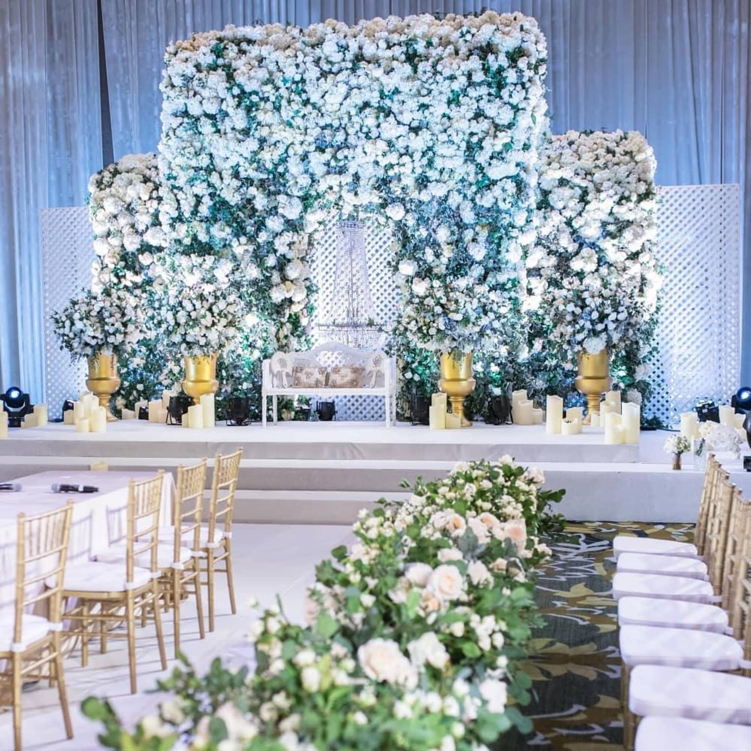 An indoor wedding reception adorned with white floral arrangements, candles and gold accents