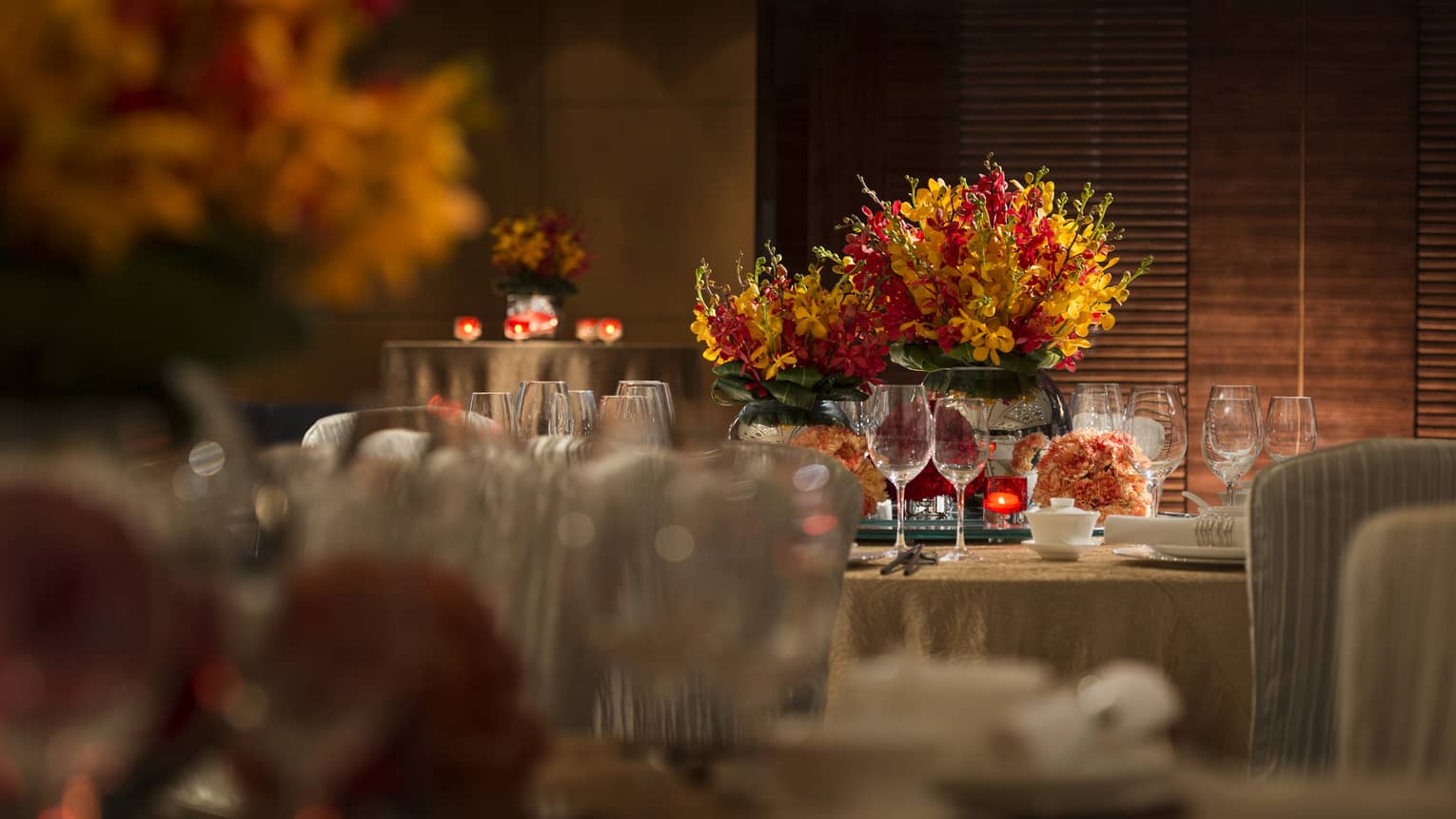 Orange and red flowers, candles on round banquet tables with gold linens