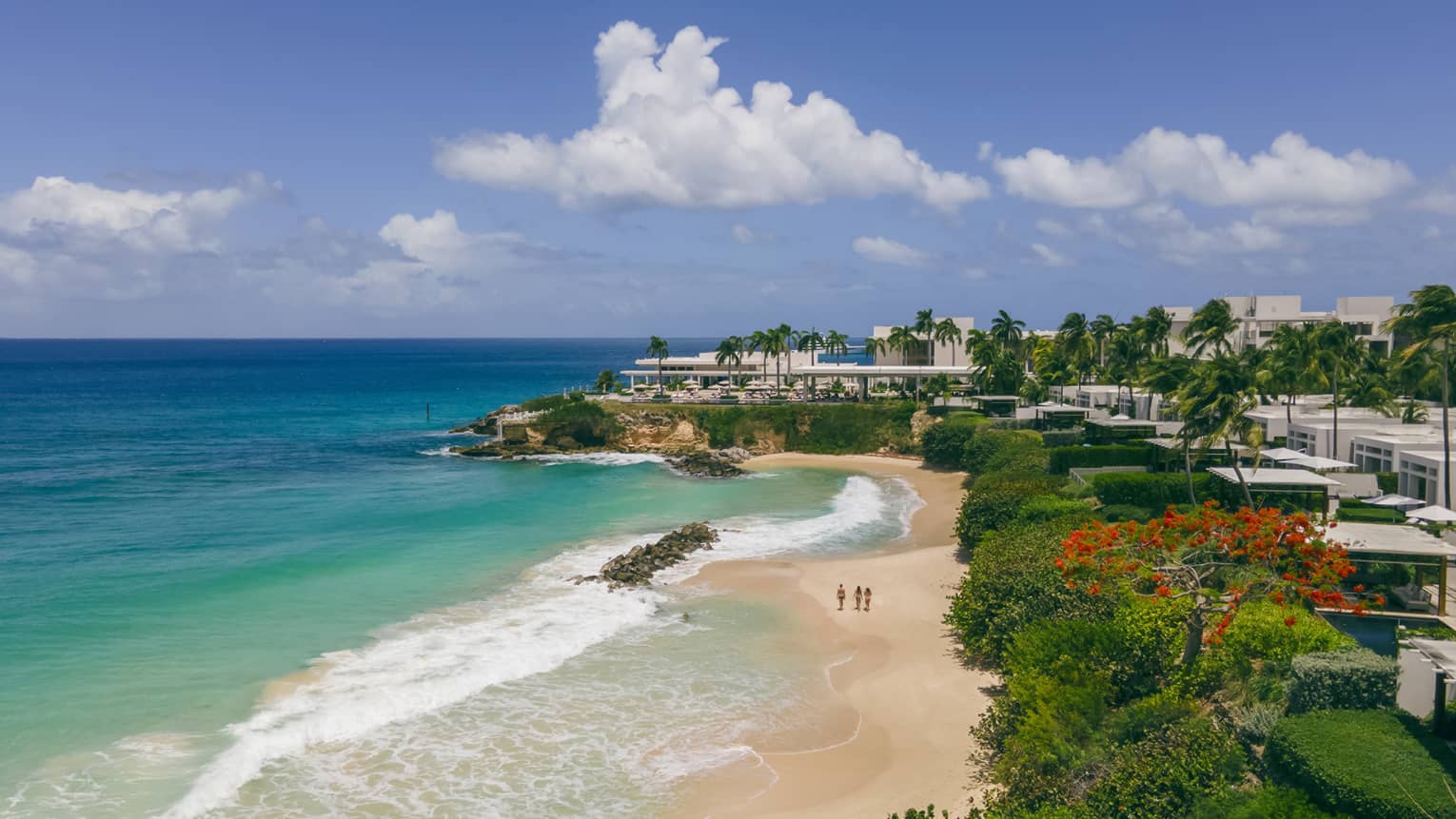 Turquoise waters and a sandy beach next to a verdant shore with structures nestled among the trees