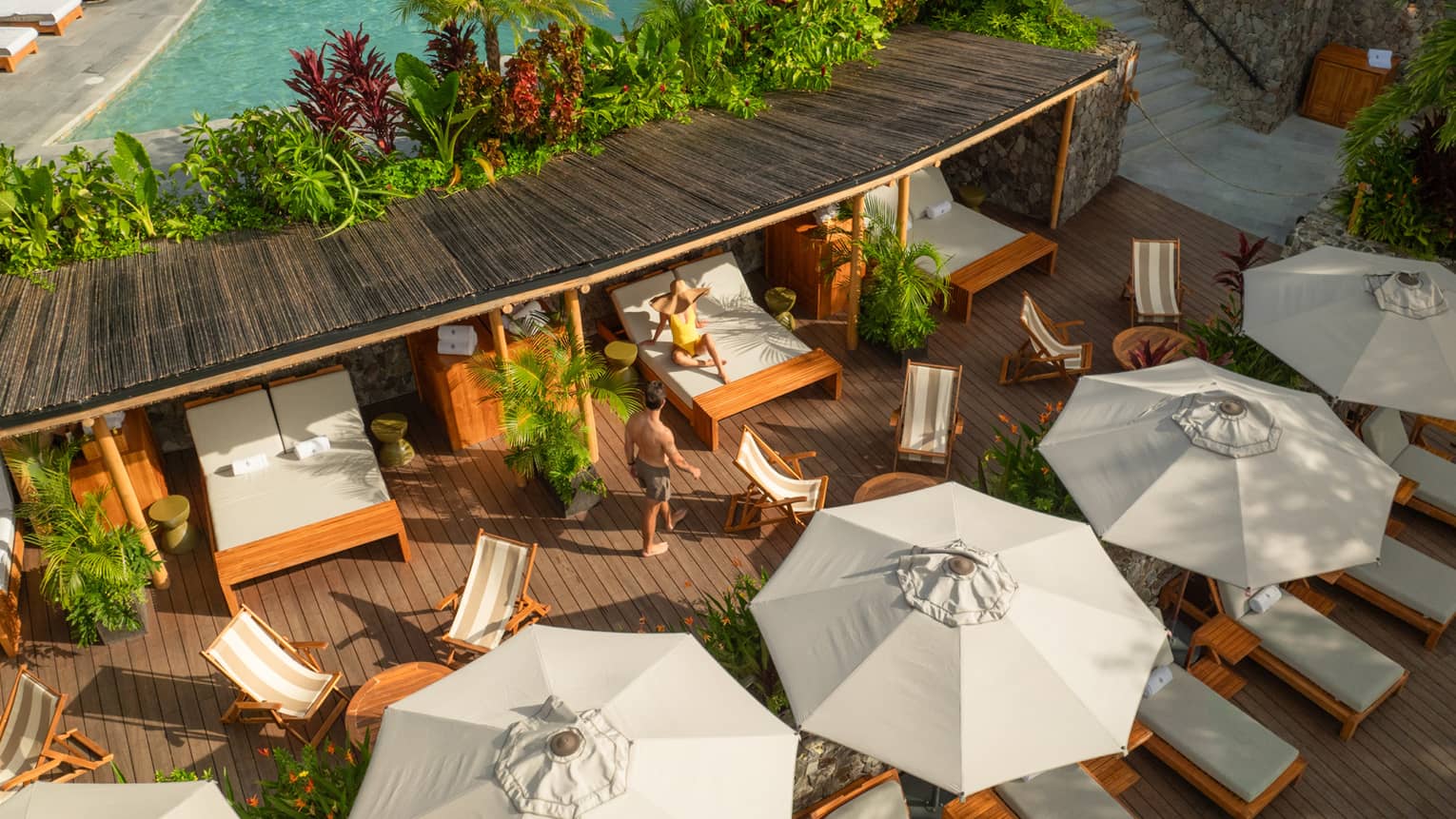Overhead view of poolside cabanas, separated by furniture and greenery and each featuring a large day bed