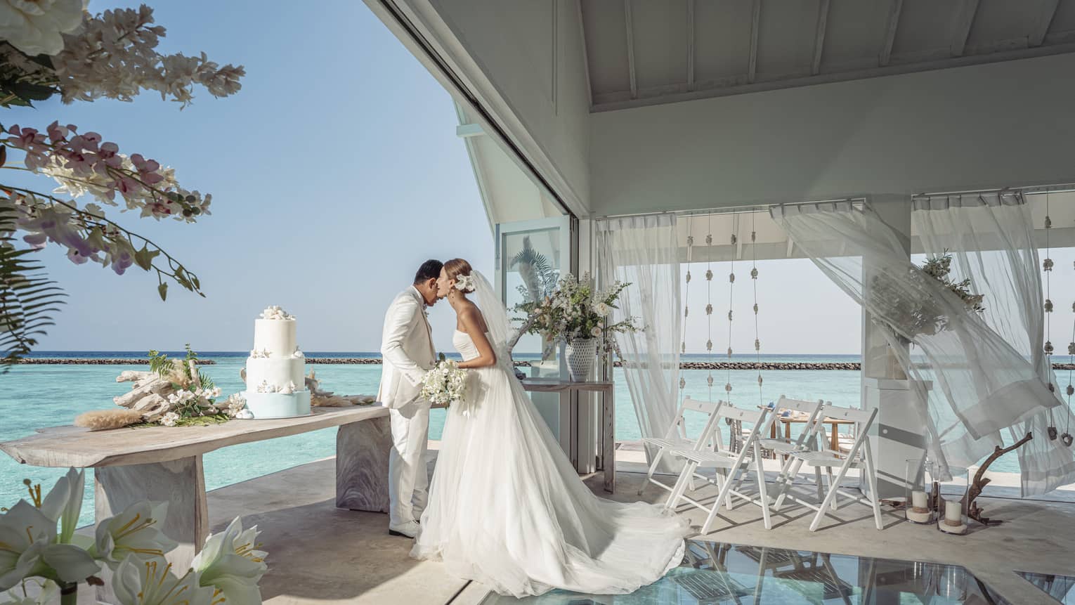 Bride whispers in groom?s ear in the glass-bottom overwater wedding pavilion
