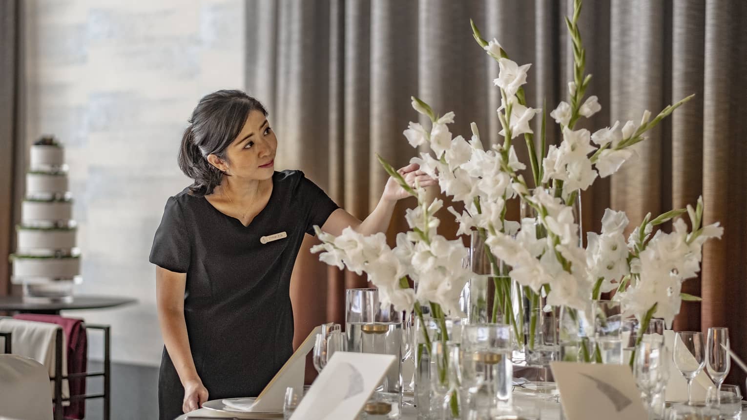 Florist tends to a large white tabletop floral arrangement in the ballroom