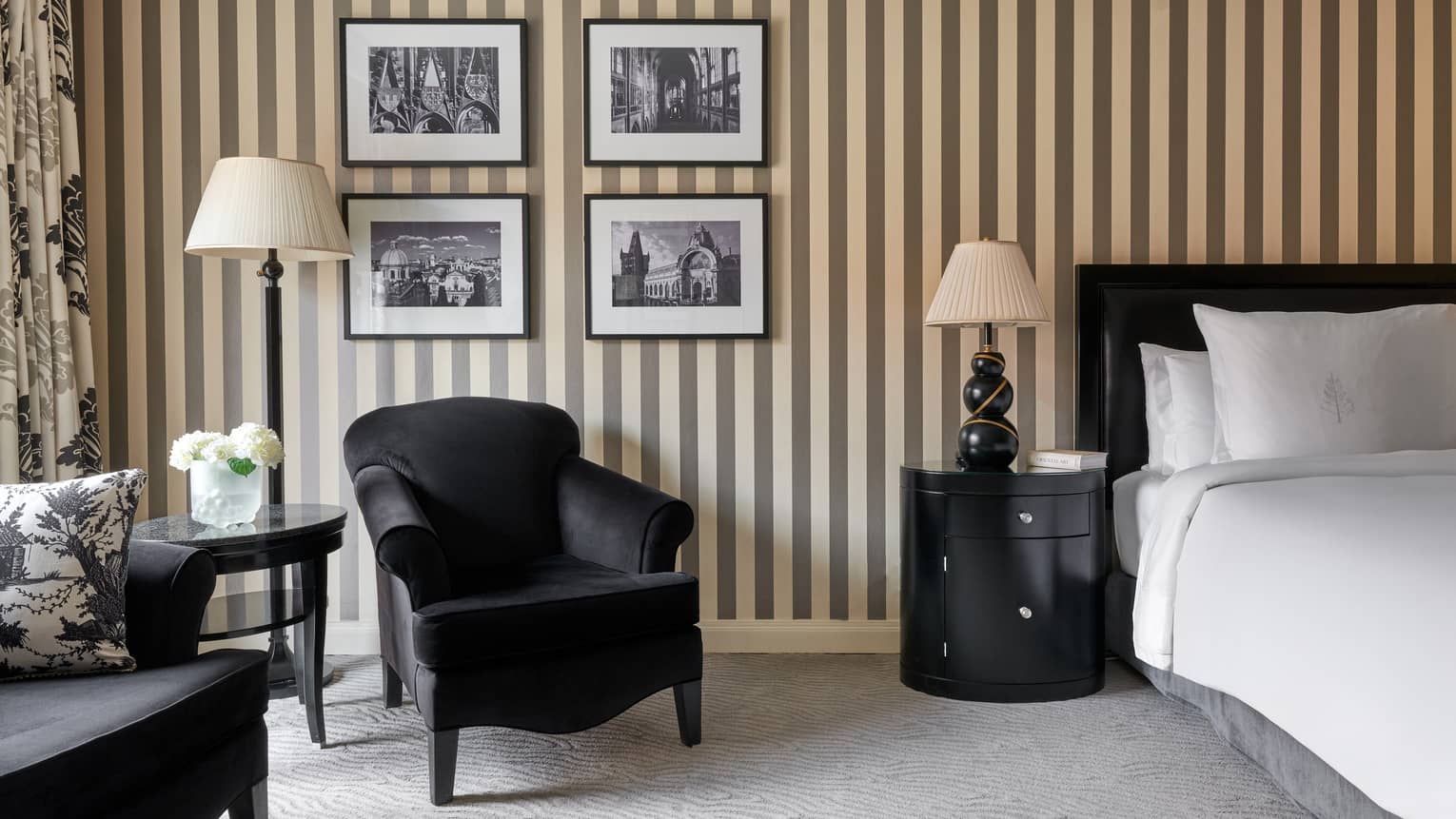 A hotel room featuring black-and-gold striped wallpaper, four framed photos, a king bed and an arm chair
