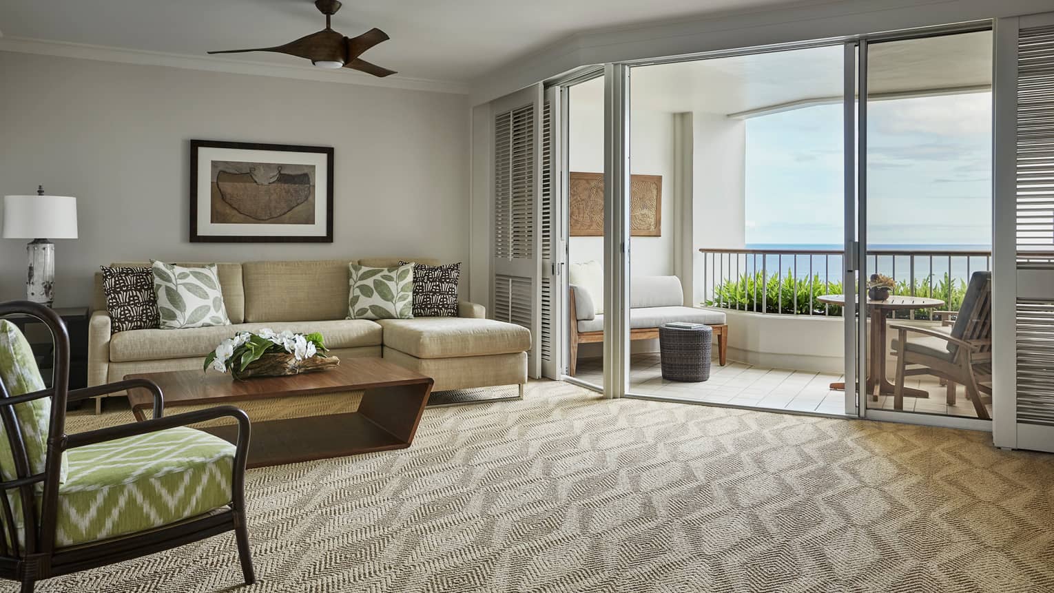 Oceanfront Suite living room with L-shaped sofa, chair on carpet, shutters on patio door