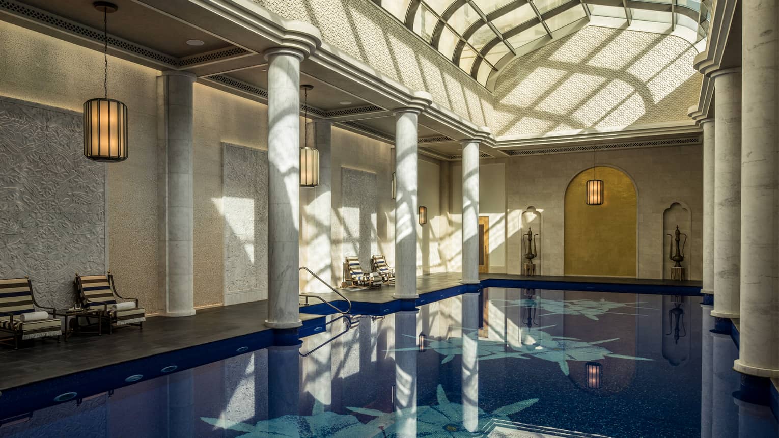 Long indoor swimming pool under curved skylights and tall white pillar columns
