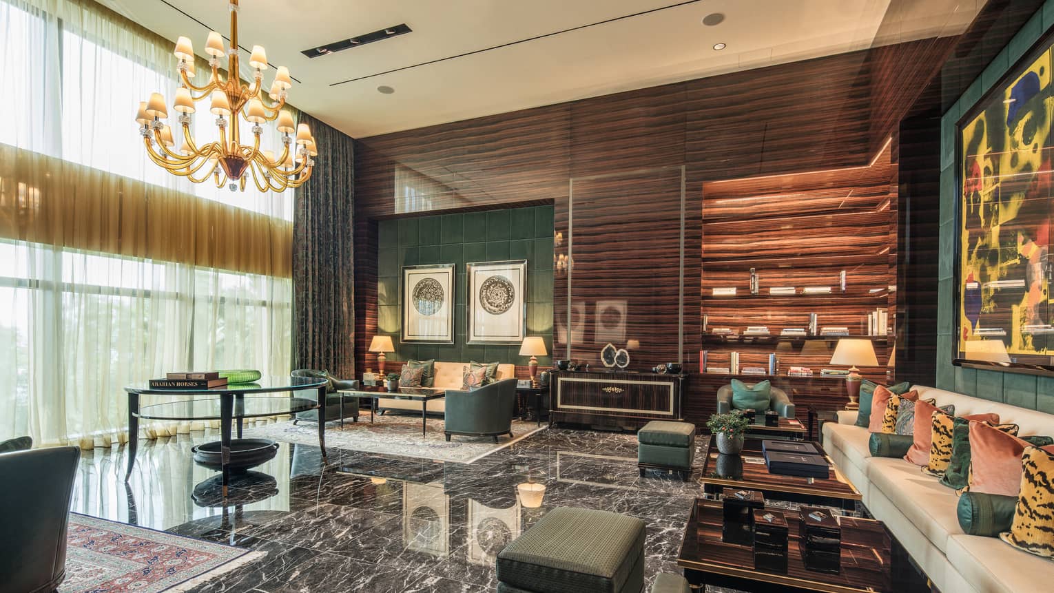 A room with a marble floor and several forest green and cream couches, all seated under a golden chandelier. 