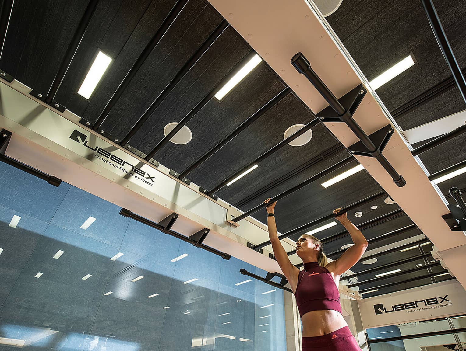 Person wearing two-piece burgundy workout outfit makes their way across a row of bars in a fitness centre