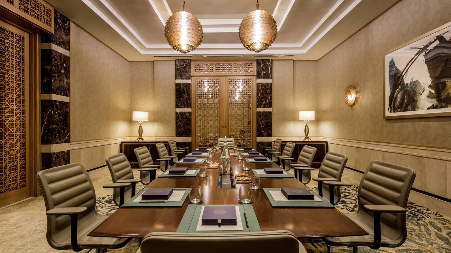 Executive table with large chairs in intimate boardroom accented with gold, ornate lights