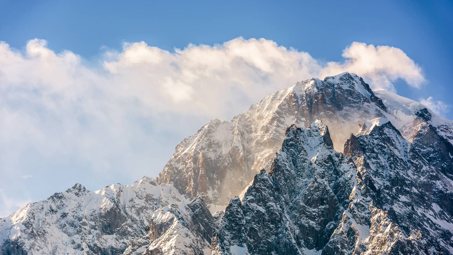 Snowy mountain peaks with blue sky and clouds in backdrop