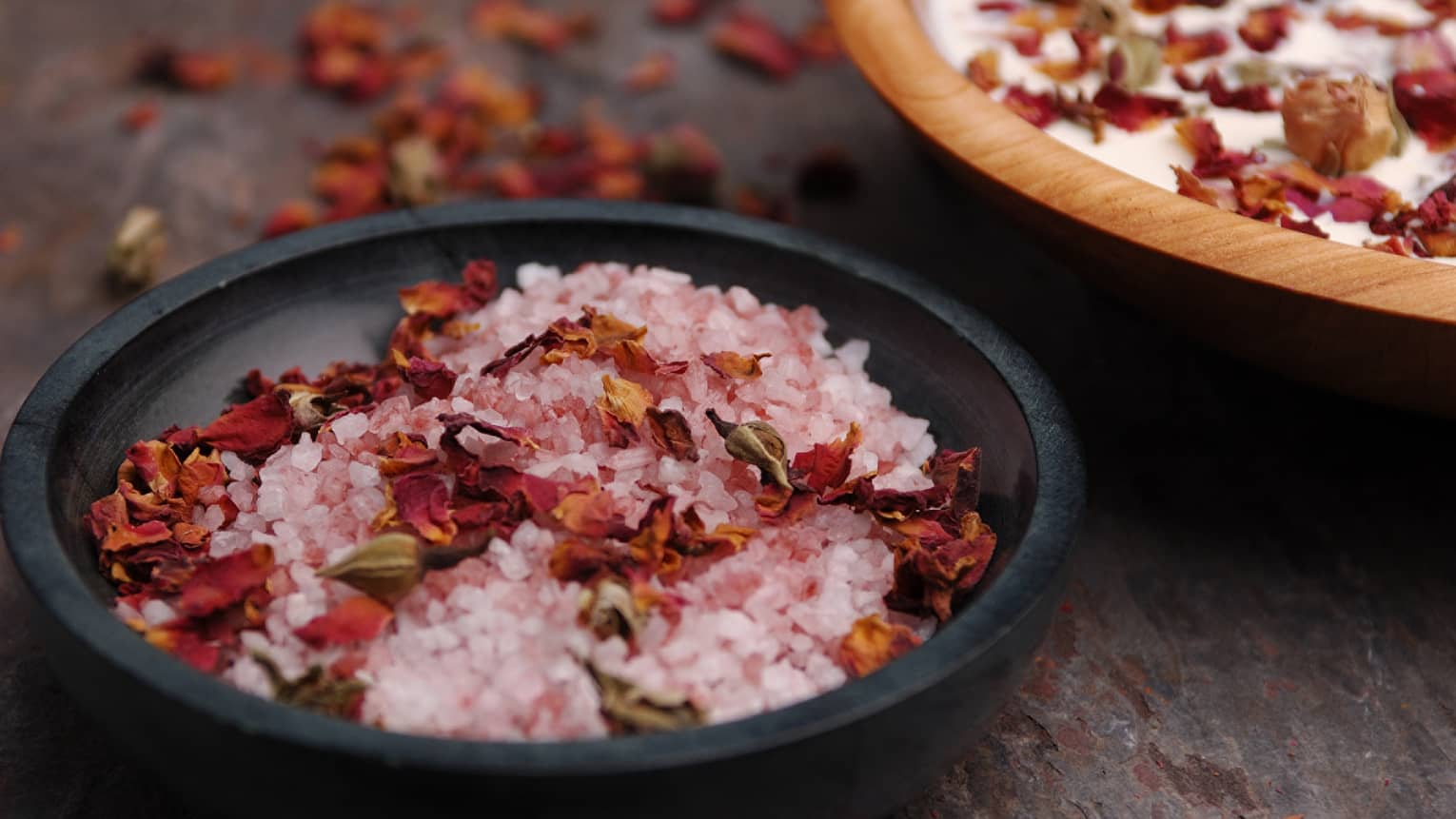 Pink crystals or salt and red flowers in a black bowl.