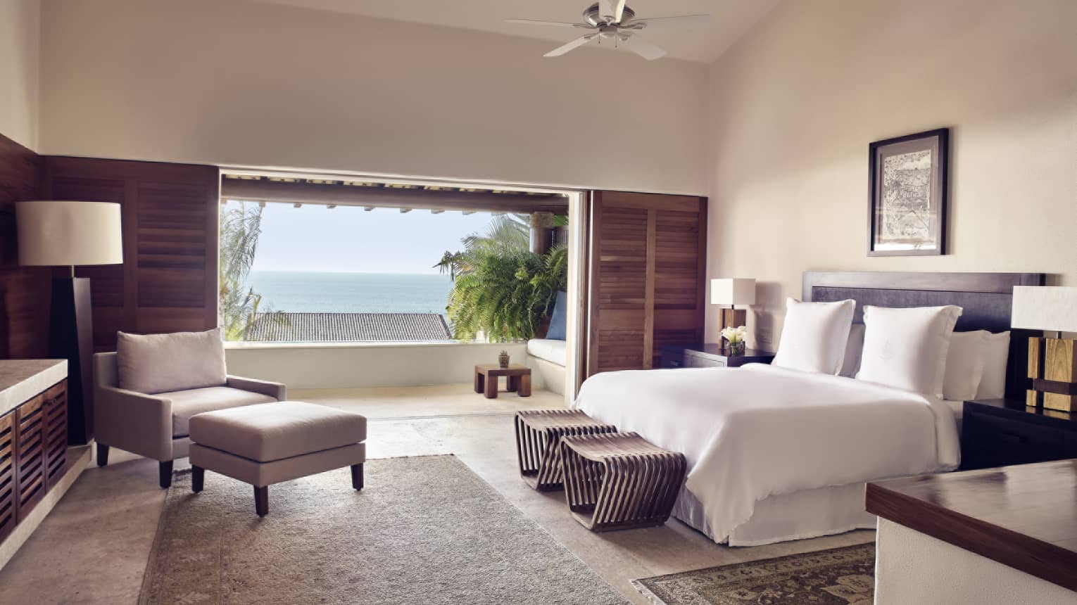 Bedroom with king bed, arm chair and ottoman and ocean-view balcony