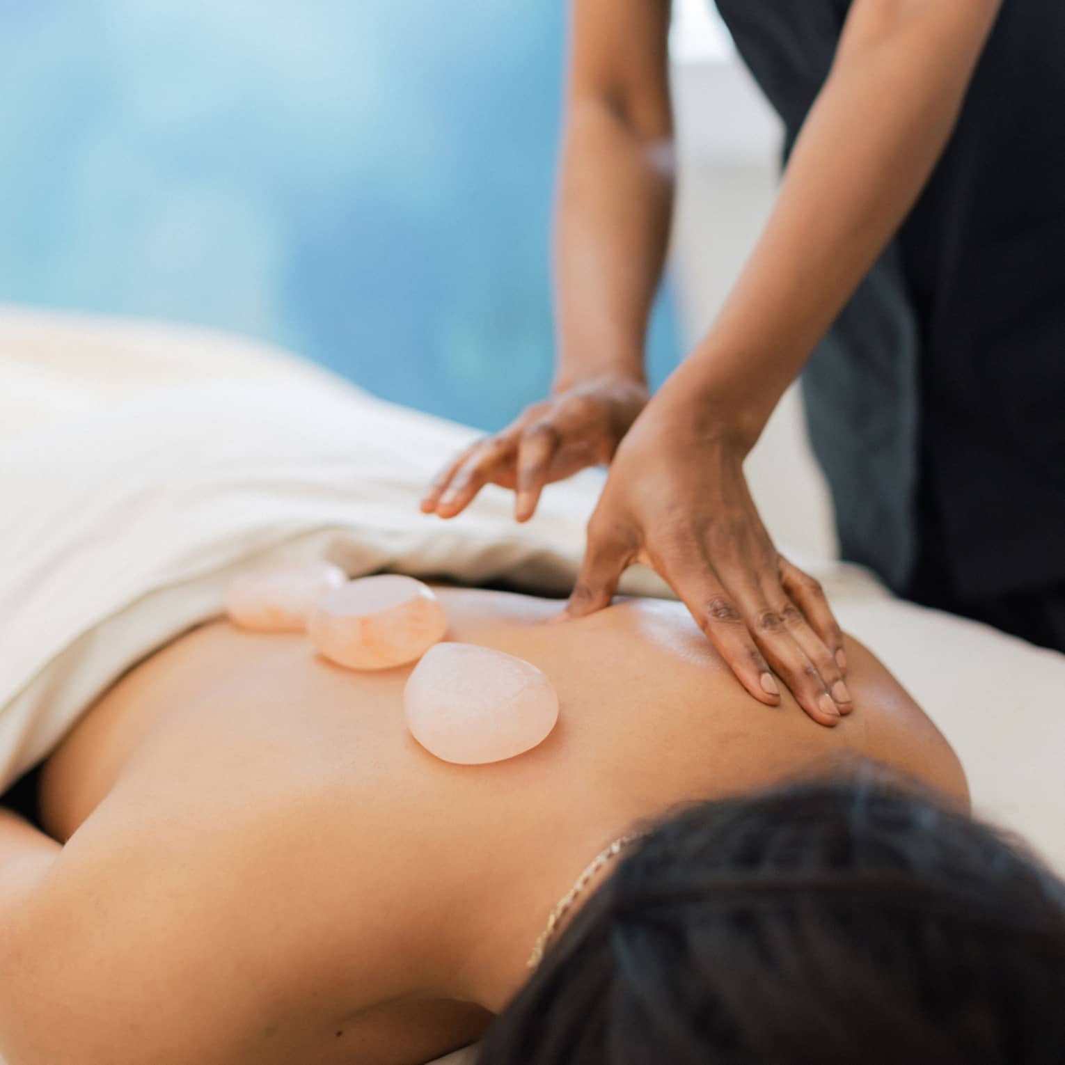 Masseuse places salt stones on a person's bare back