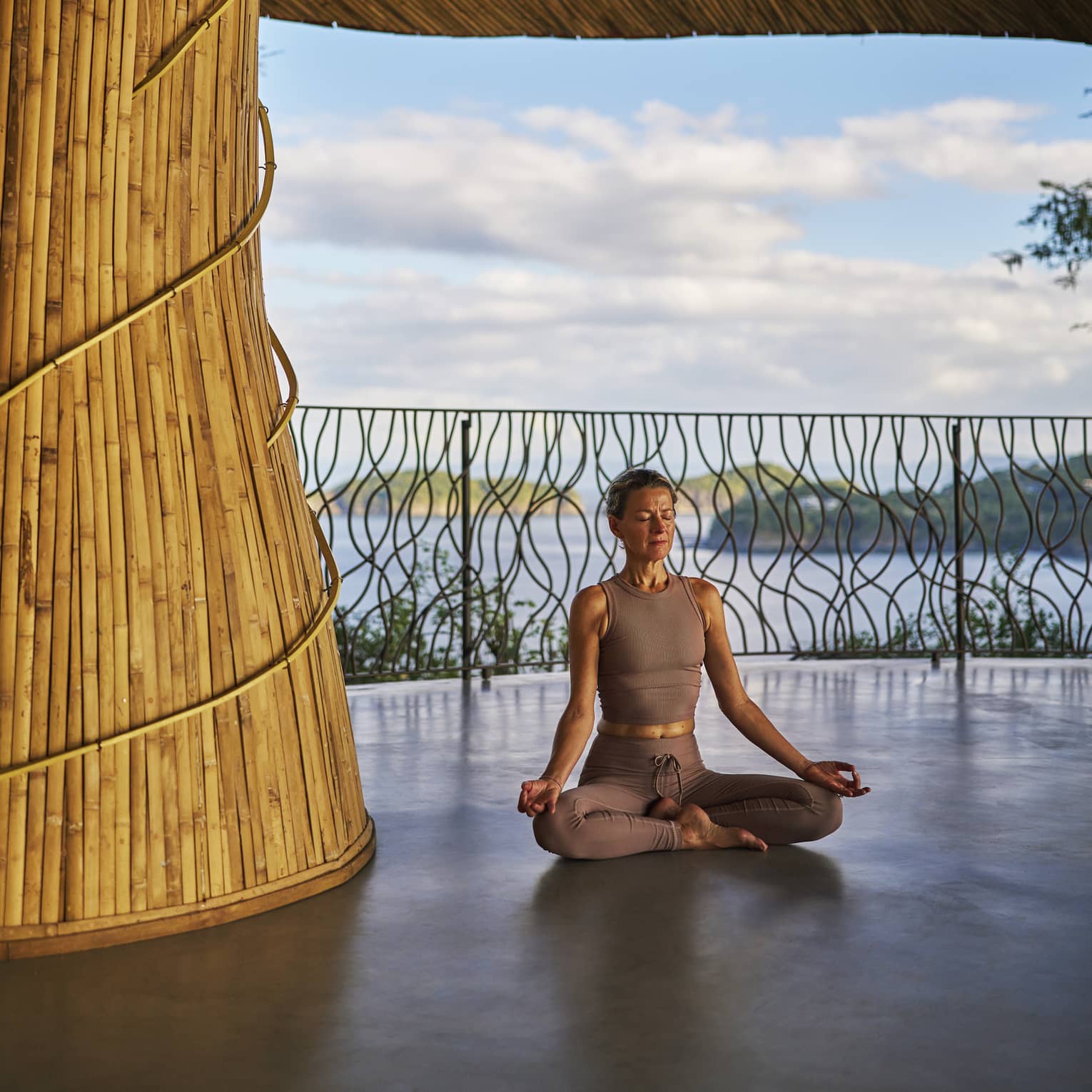 Person sits cross-legged inside an open-air wellness shala with the sea in the background