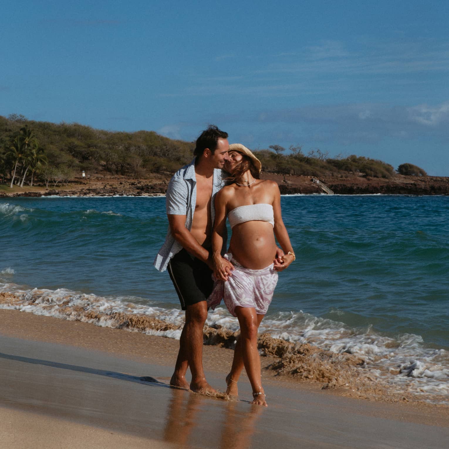 Man and pregnant woman walk together and embrace on the beach