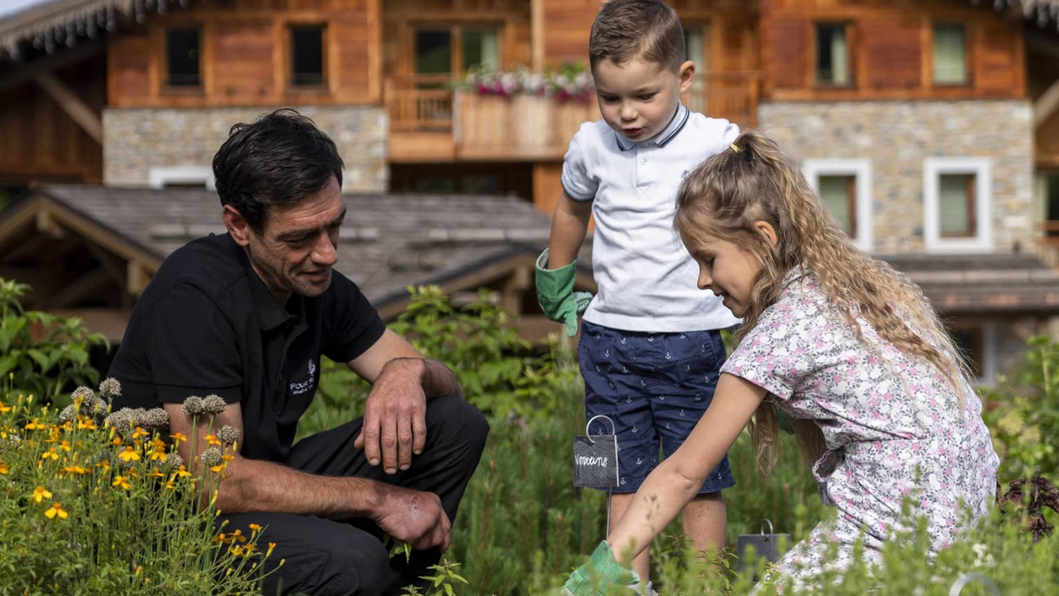 Man kneeling in meadow with two children with chalet in backdrop