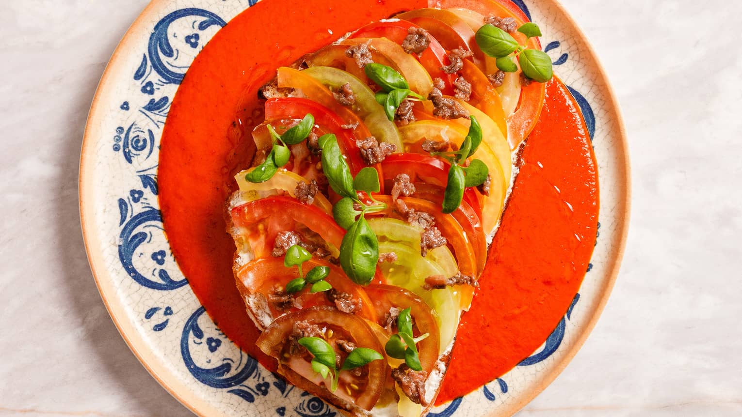 Slice of bread topped with slices of red and yellow tomato and anchovies