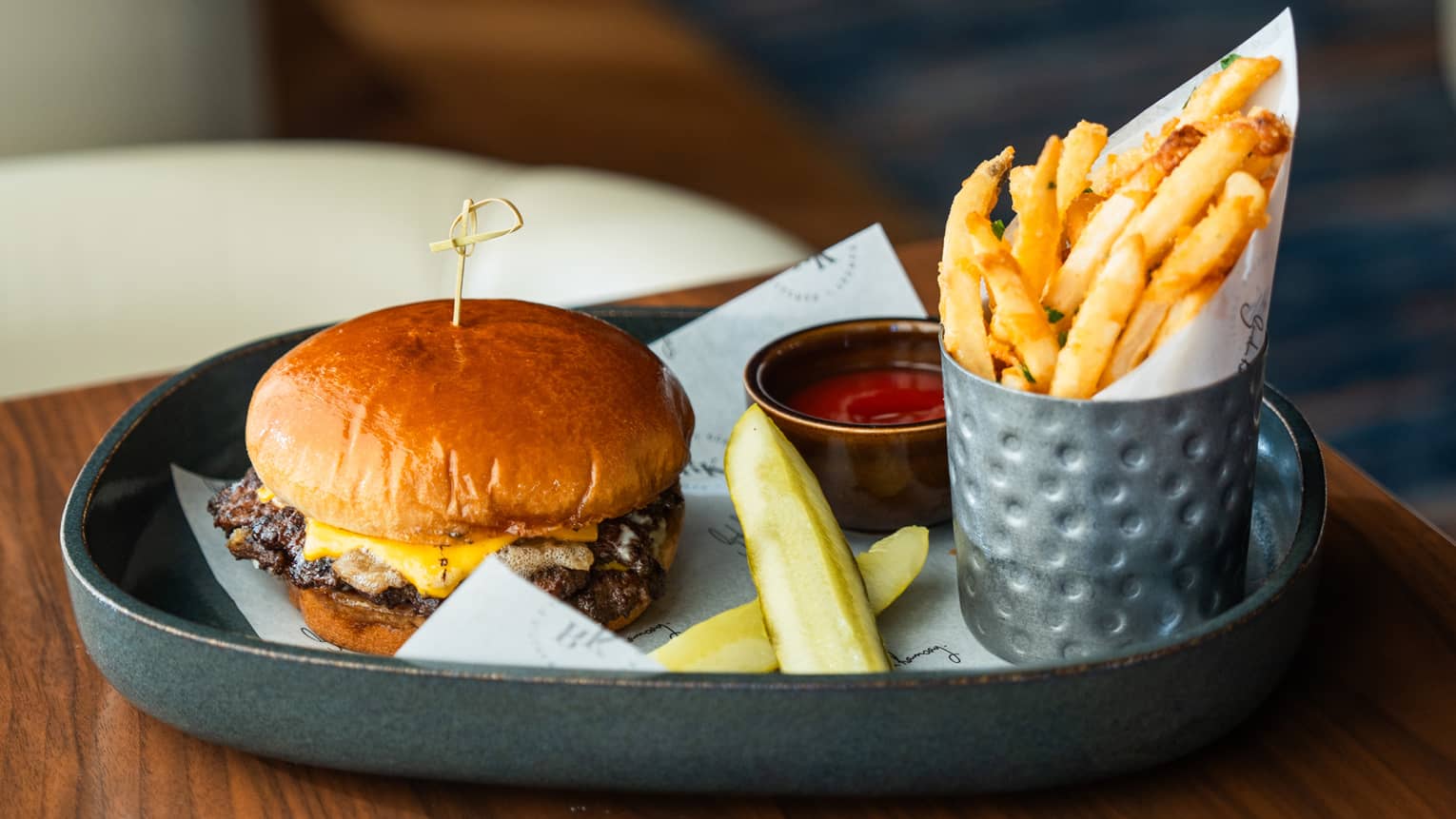 A cheeseburger, pickle slices, fries and ketchup served in a gray ceramic dish