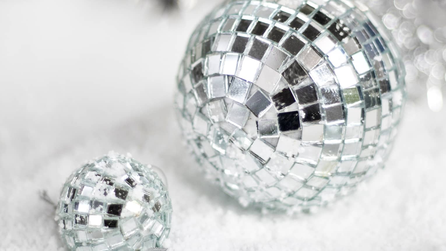 Small ornaments that looks like disco balls, spheres covered in small mirror, are laying on white fabric.
