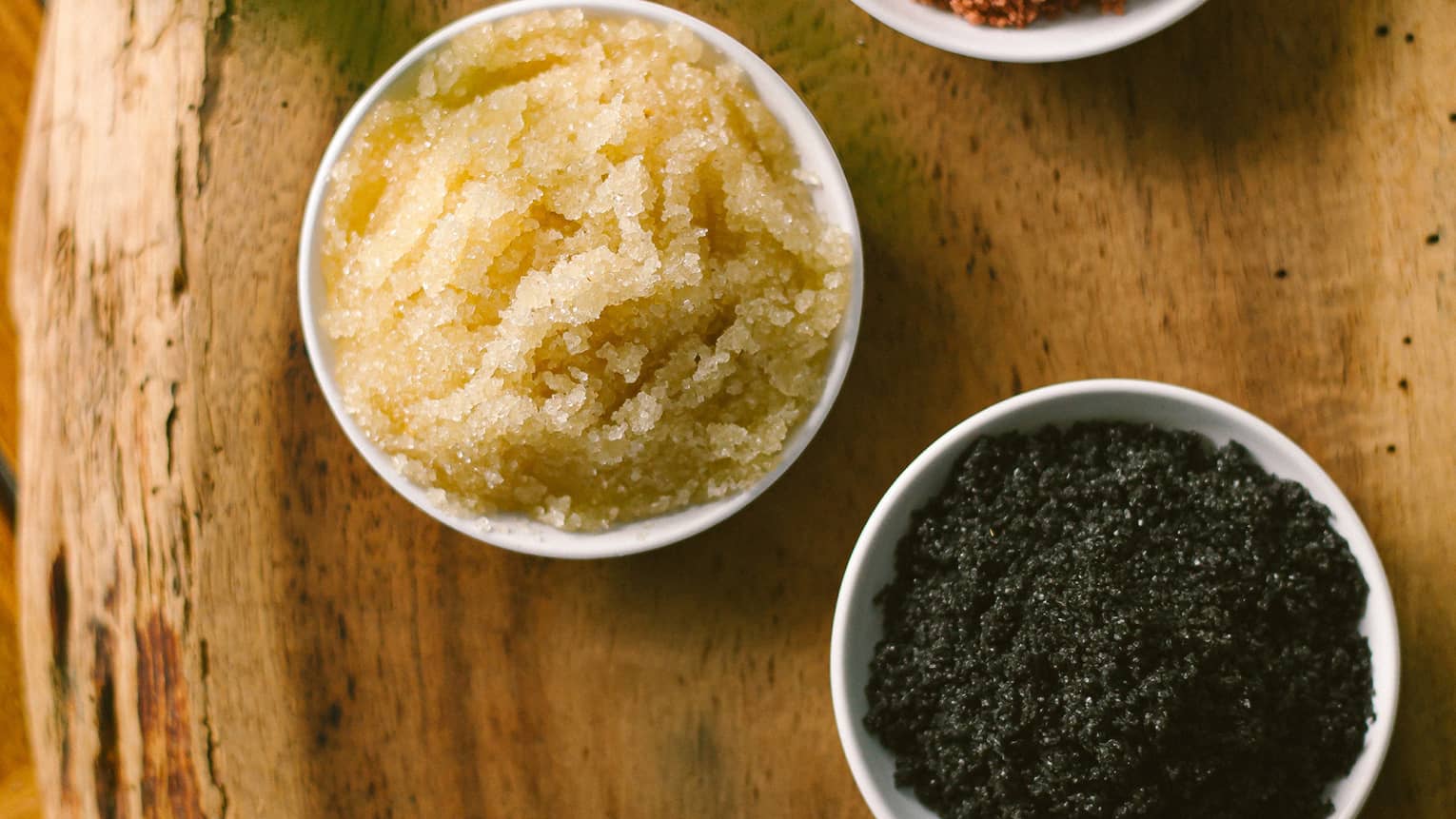 Aerial view of three dishes with salt scrubs on rustic wood platter