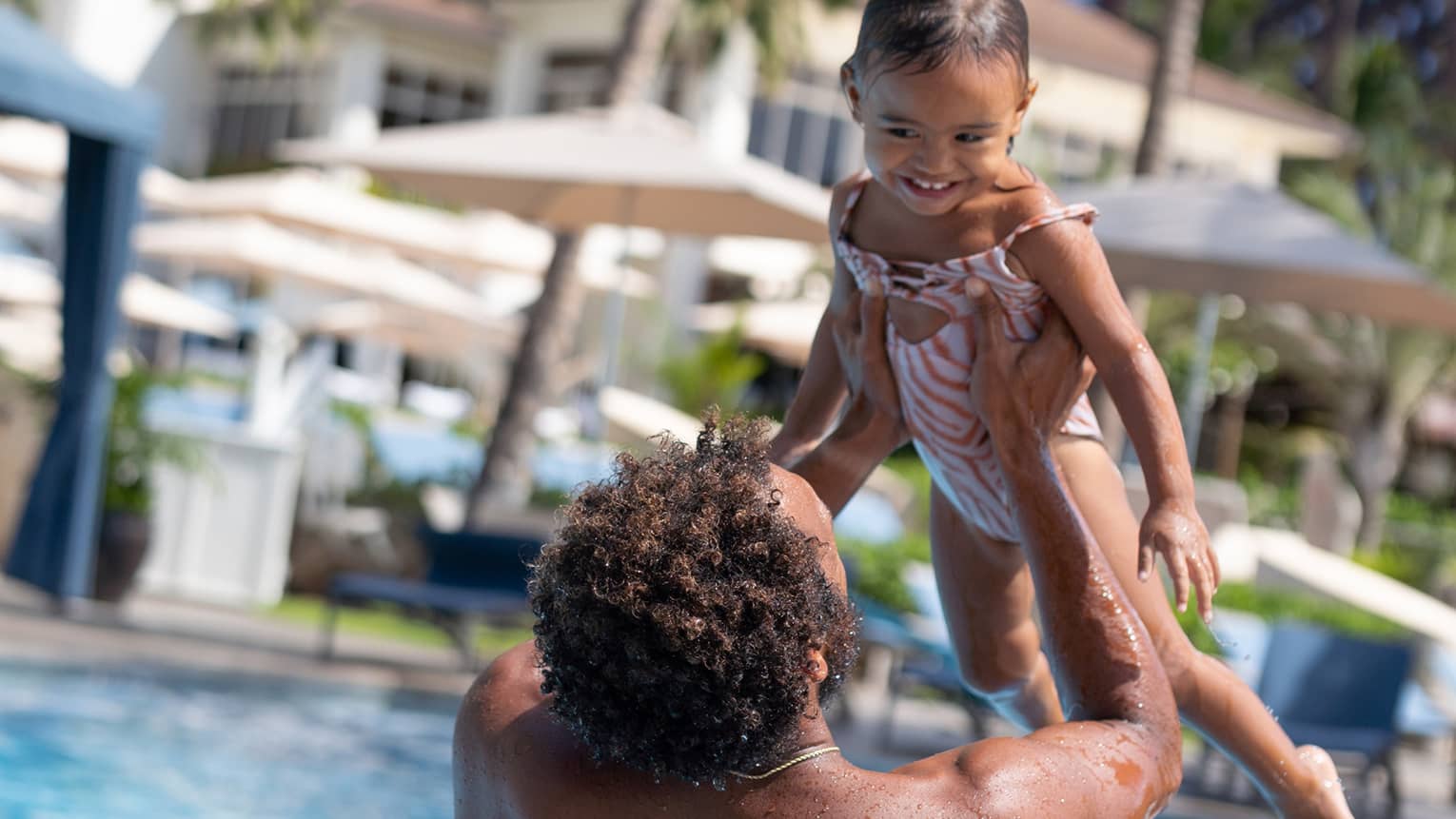 A man lifts a young girl up in a resort pool