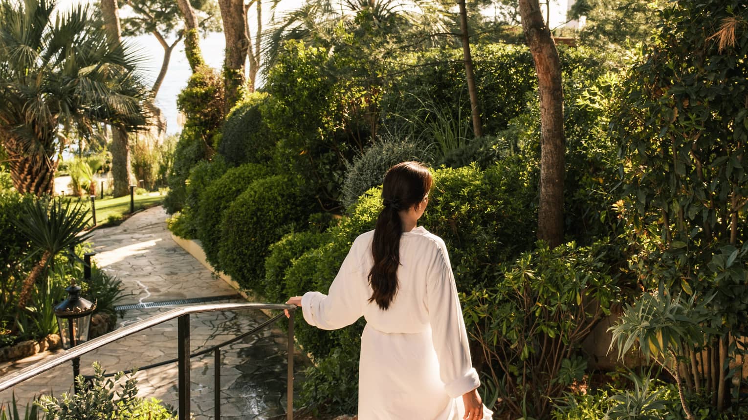 A woman walks in a white spa bathrobe through gardens