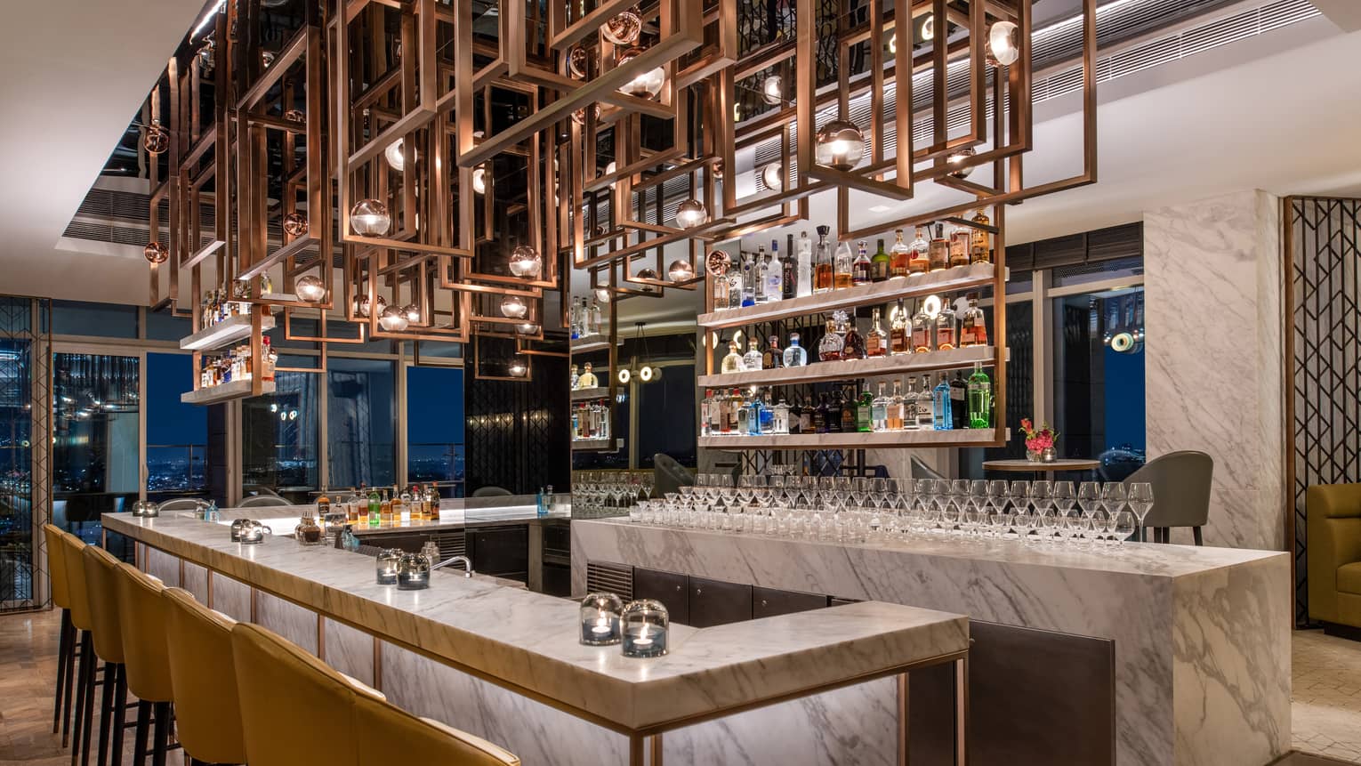 Marbled bar area with mustard-coloured chairs, ornate metal sculpture above head and liquor bottle display