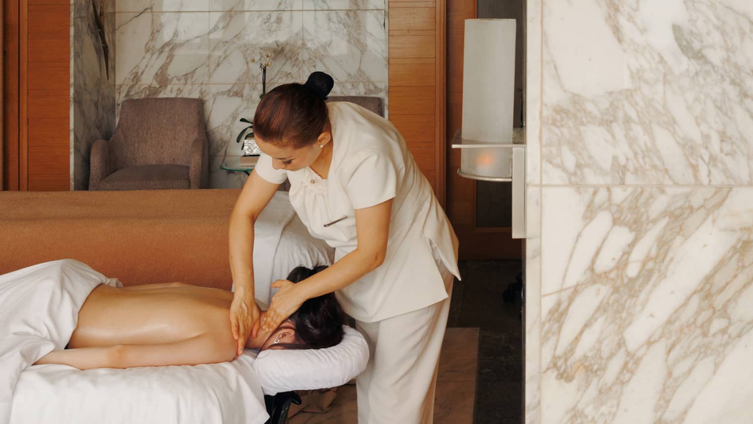 A female spa therapist performing a massage on a woman, face down on spa treatment table, in a chic luxury spa with marble walls