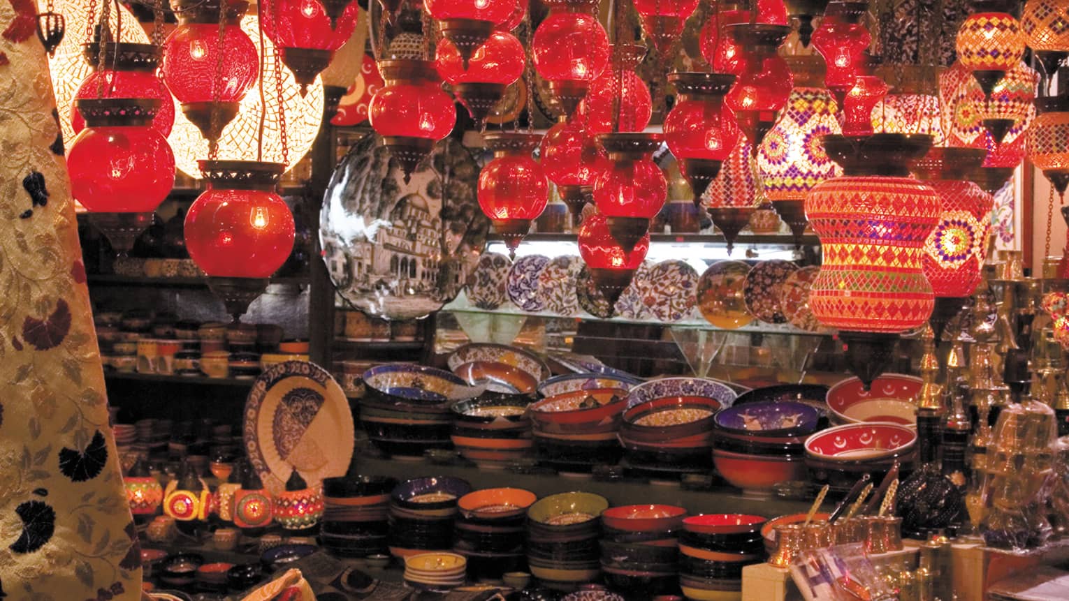 Red lanterns hang over shelves with decorative plates in Grand Bazaar