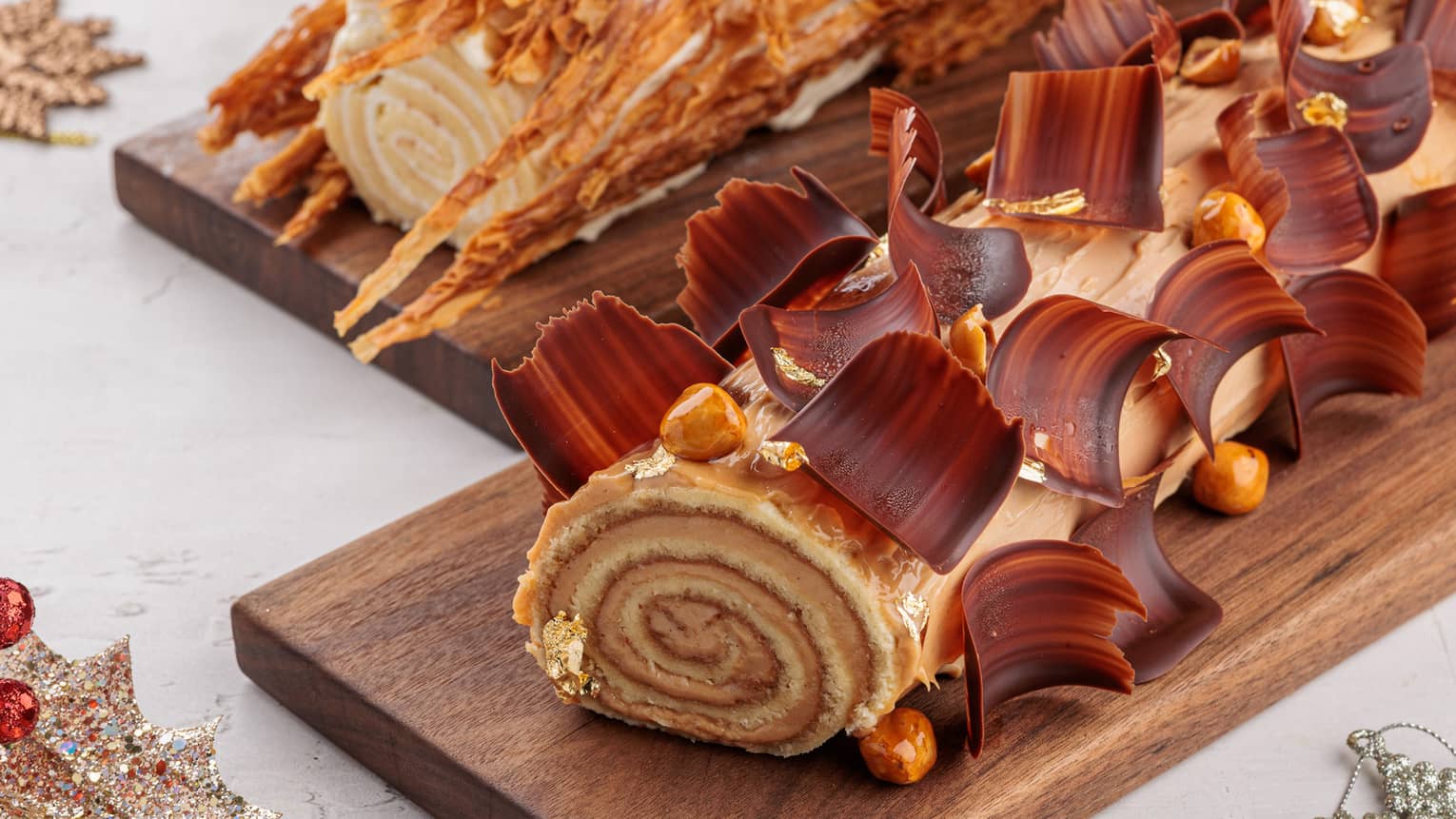 Two decorative yule logs displayed on dark-brown rectangular wooden platters