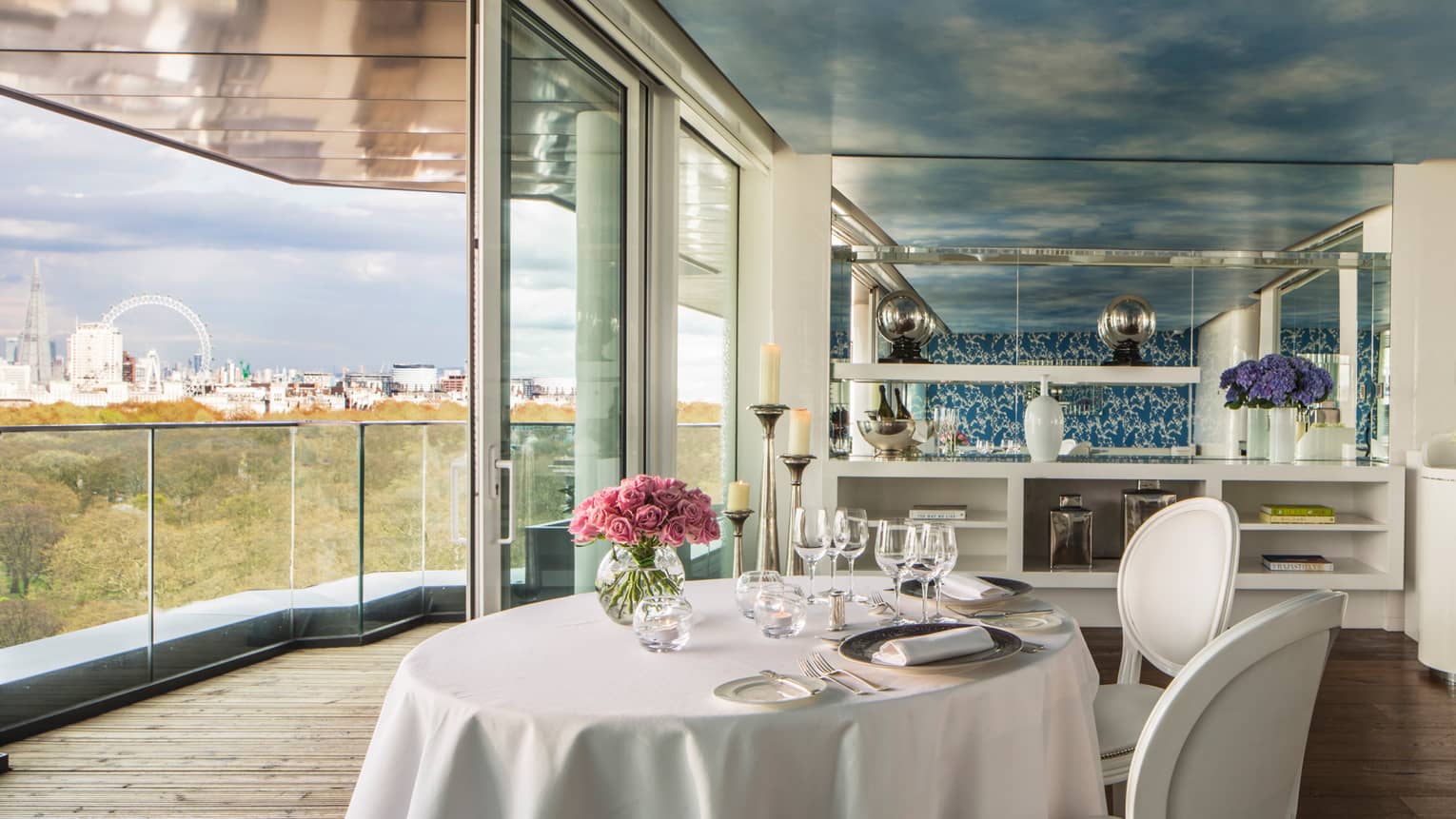 Amaranto restaurant, round dining table with white linens pink roses by open wall, glass balcony