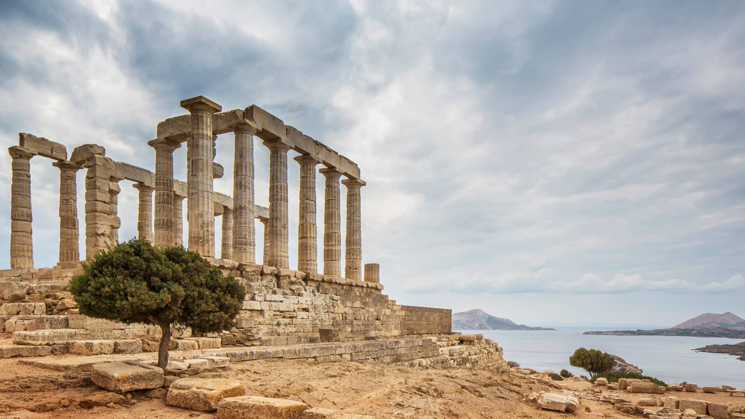 Ancient ruins stand near water under sky with clouds
